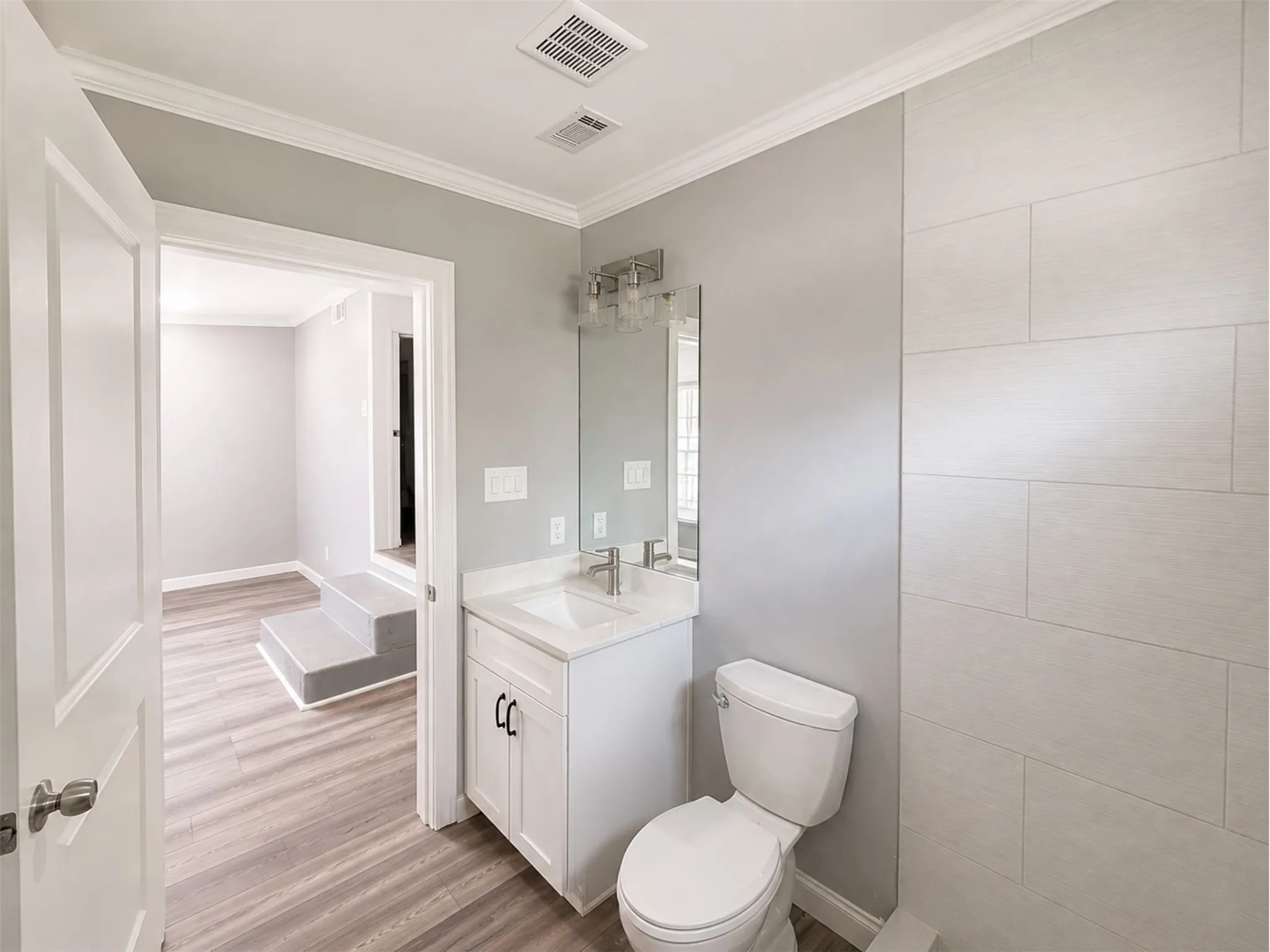 Bathroom featuring a single vanity with storage, a rectangular mirror, a toilet, a tiled shower wall, and wood-finish flooring