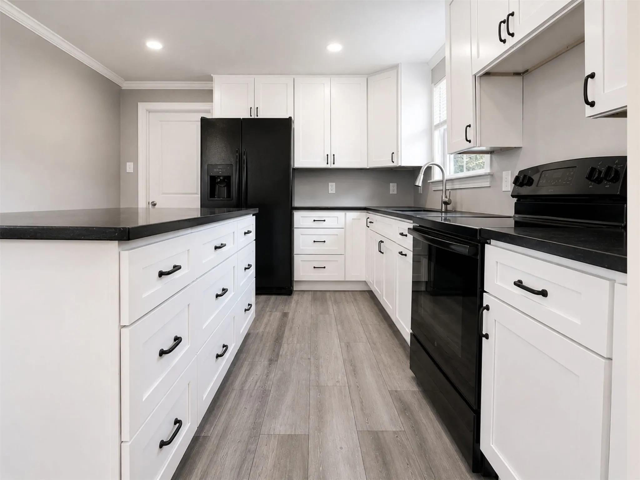 Kitchen featuring white shaker-style cabinetry, dark countertops, a large island with drawers, black appliances, and wood-finish flooring