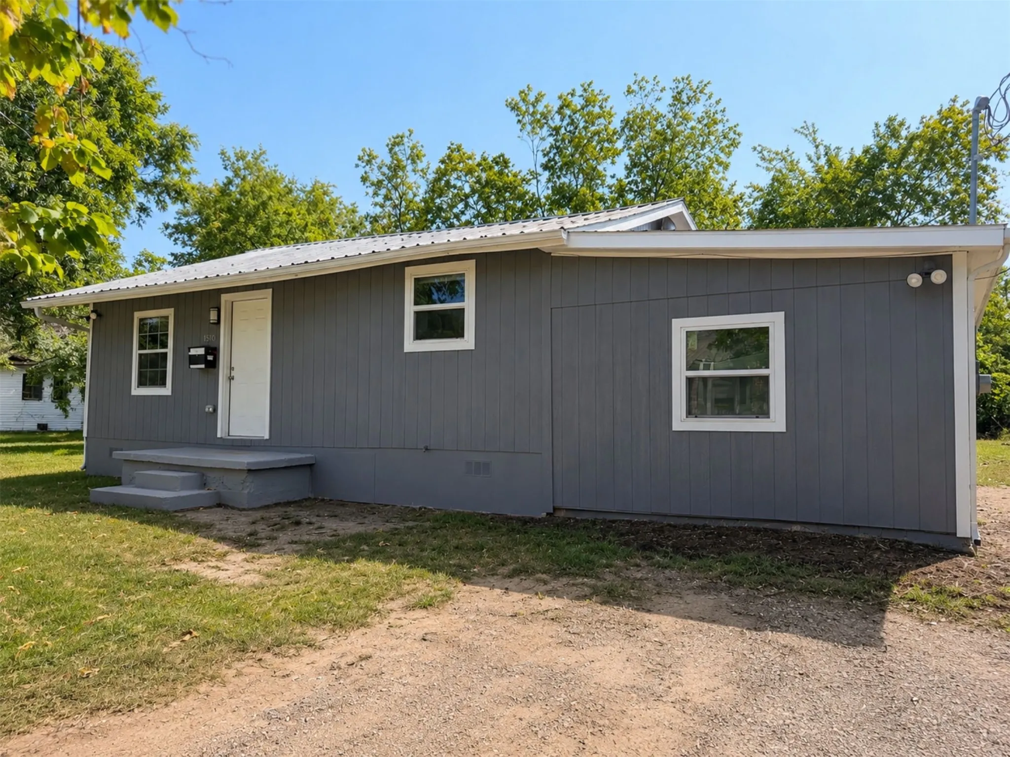 Gray vertical siding with white trim, a white entry door, and a metal roof