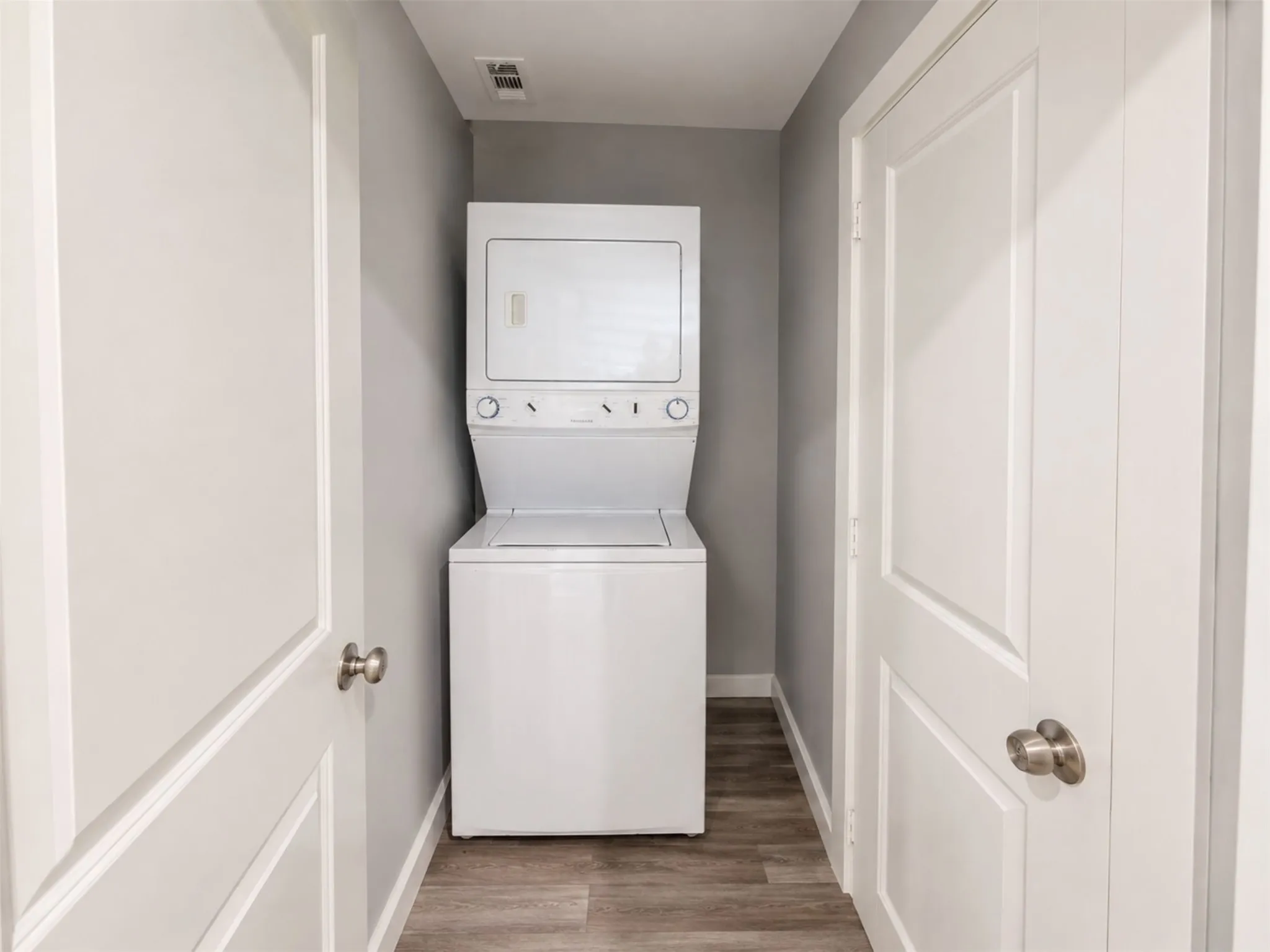 Stackable washer and dryer unit, wood-finish flooring, white panel doors, and neutral gray wall paint