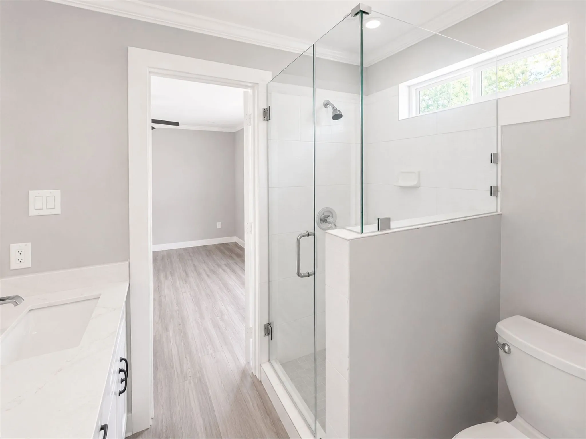 Glass-enclosed shower with subway tile surround, sleek vanity with a rectangular undermount sink, and wood-finish flooring