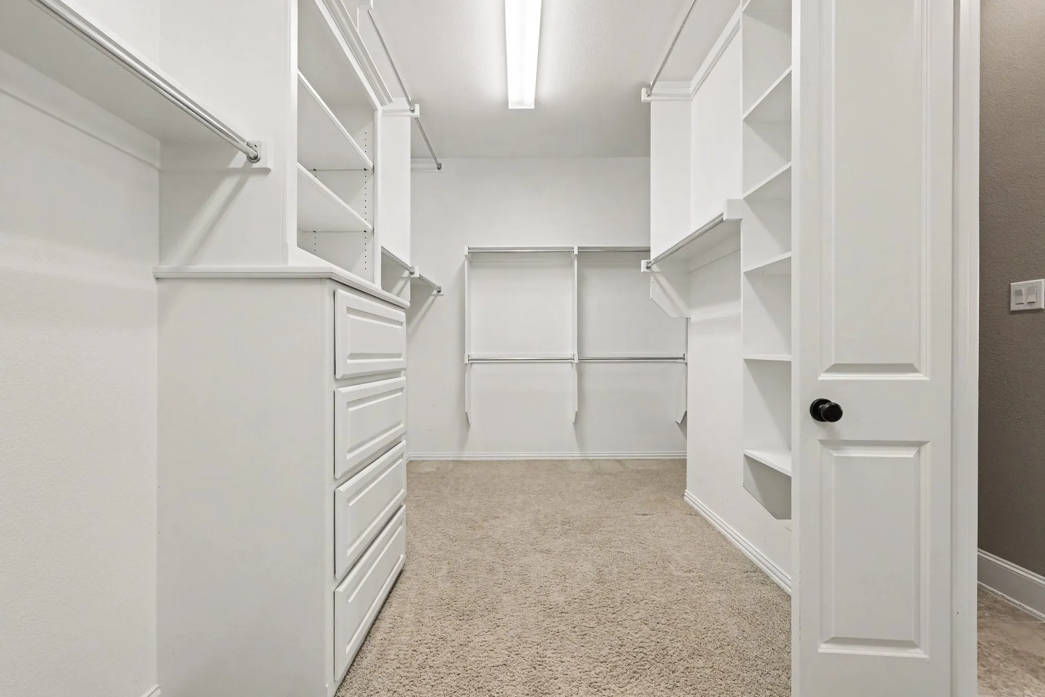 Walk-in closet featuring white built-in shelving, hanging rods, and a four-drawer dresser