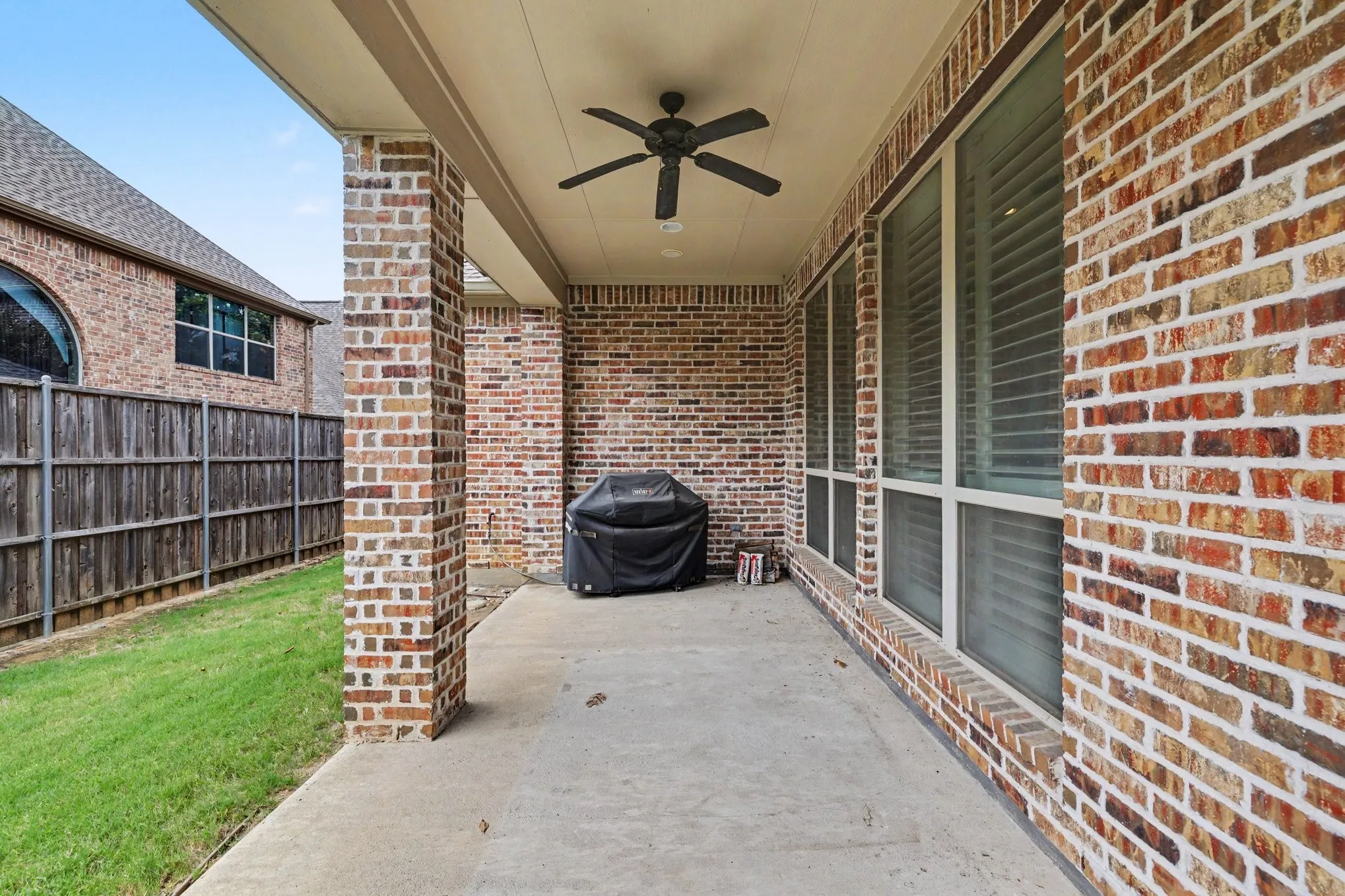 Covered patio with a ceiling fan, brick exterior, and a privacy fence