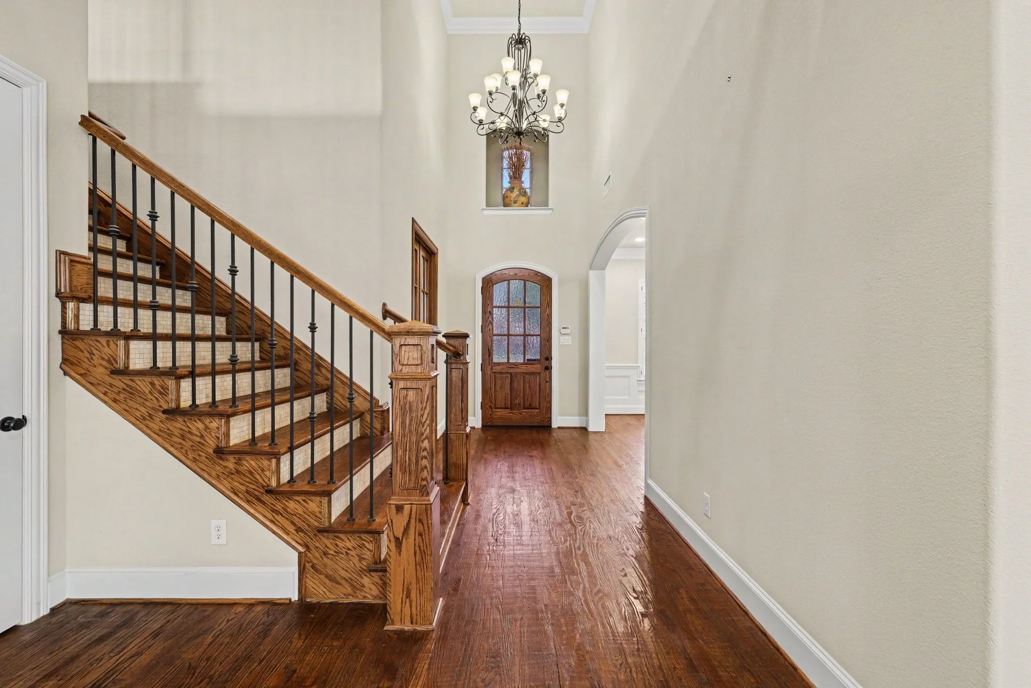Hardwood flooring, wood staircase with iron balusters, arched doorway, wood entry door with glass panels, and a high ceiling