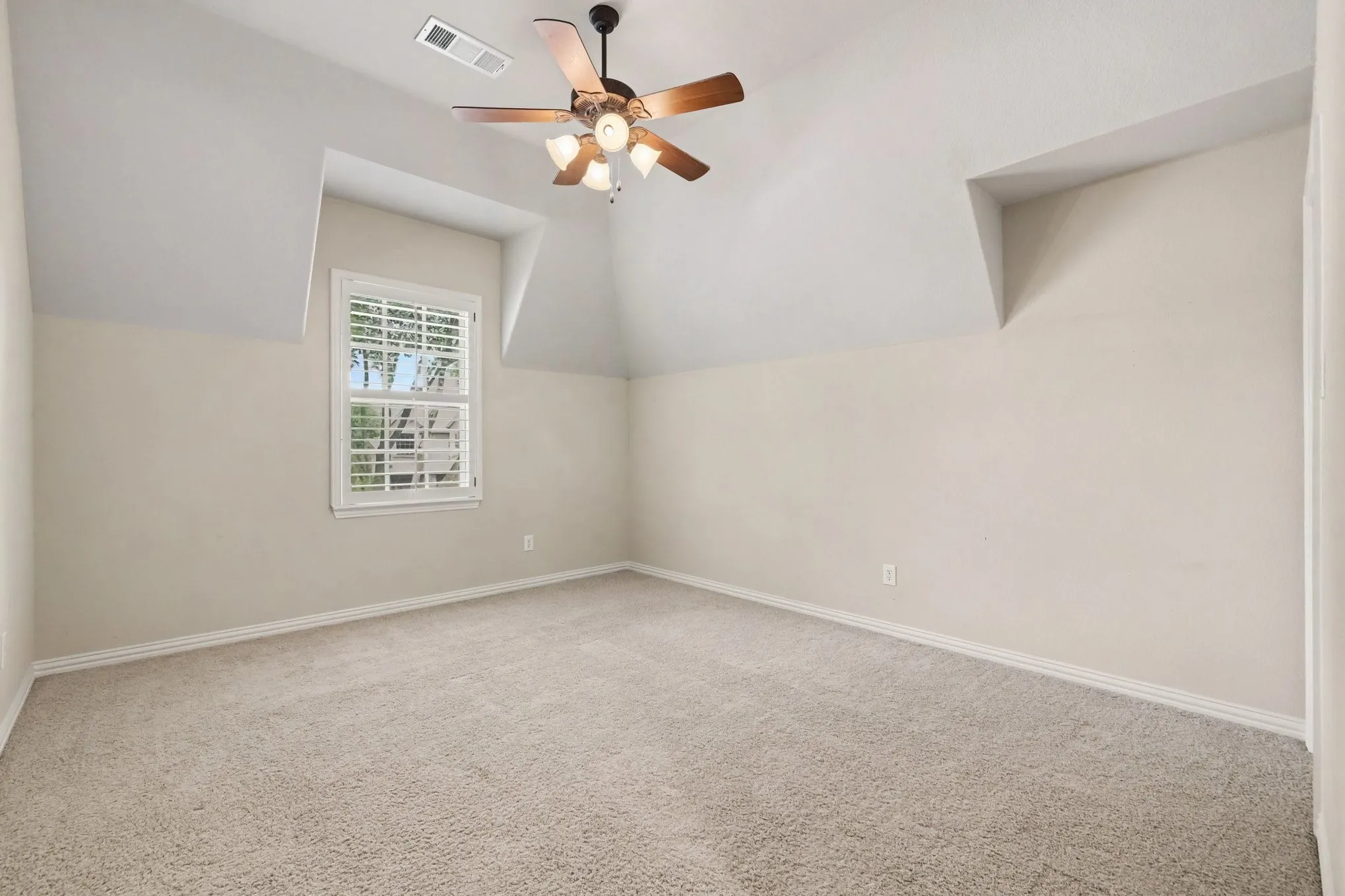 Vaulted ceiling with a ceiling fan, plush carpet flooring, window with shutters, and architectural dormer details