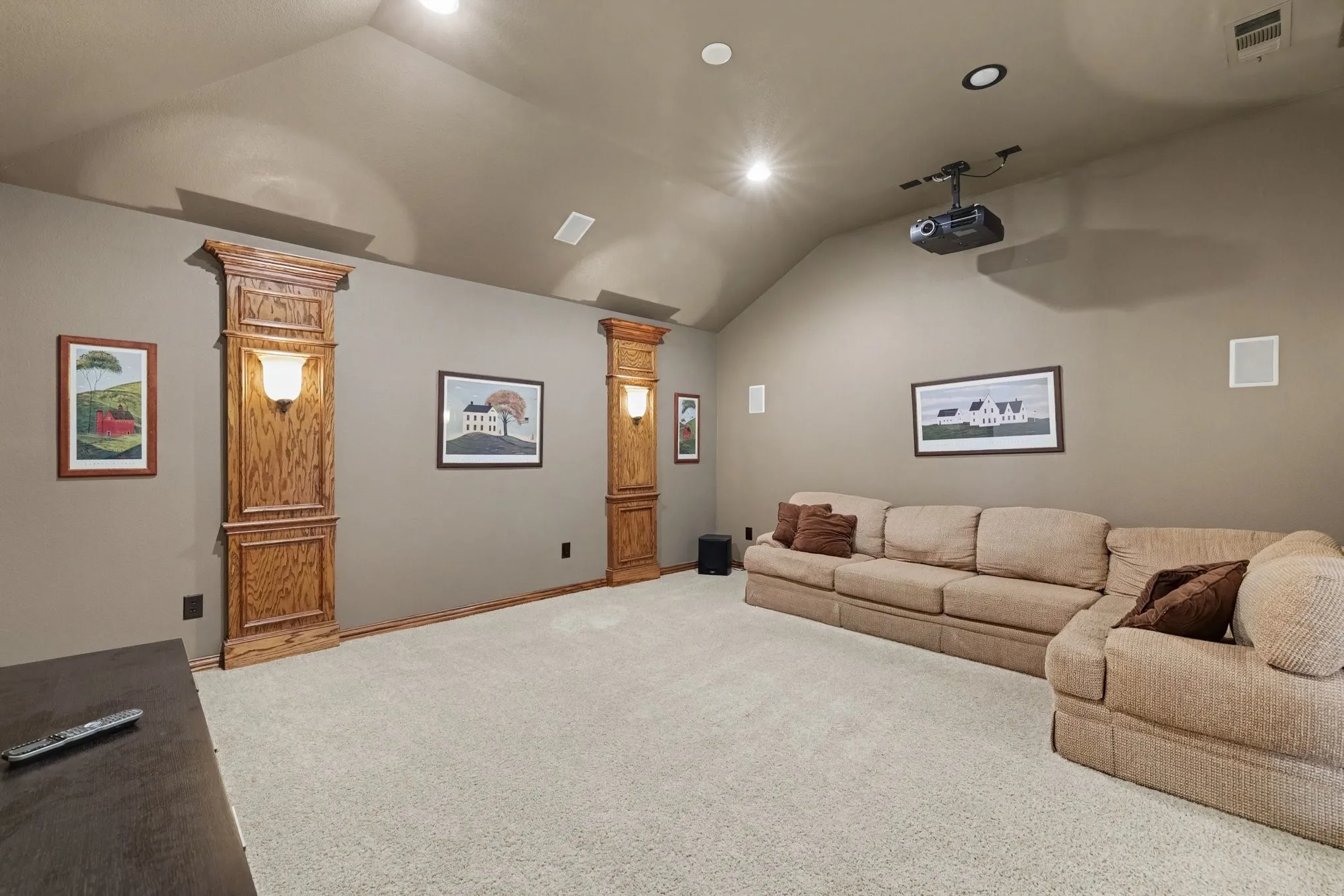 Vaulted ceiling, recessed lighting, built-in wall sconces with wood-finish trim, wall-mounted speakers, and ceiling-mounted projector