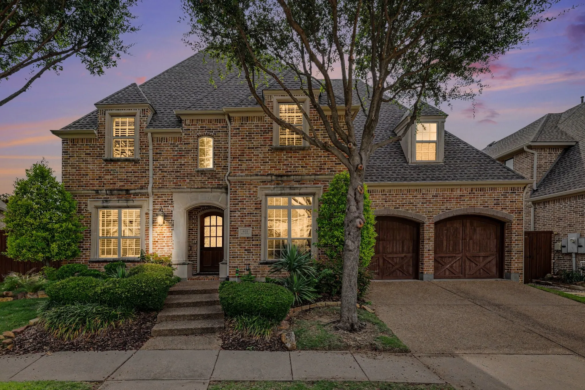 Brick exterior with stone accents, arched entry, dark wood front door, and two-car garage with arched wood doors