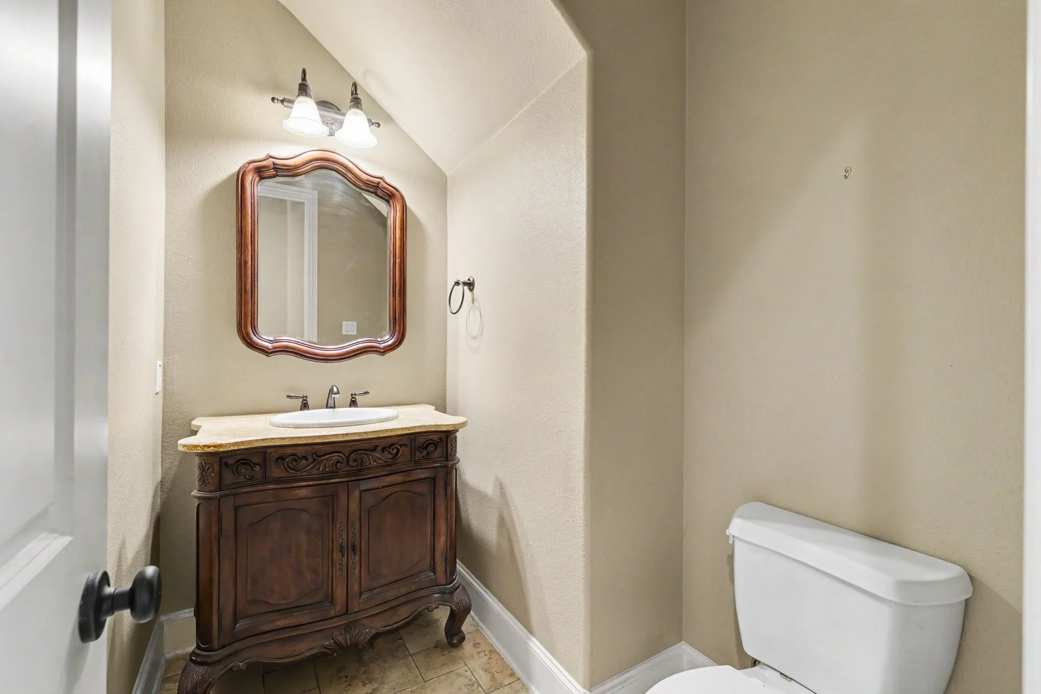 Ornate vanity with integrated sink, framed mirror, wall-mounted light fixture, and tiled flooring