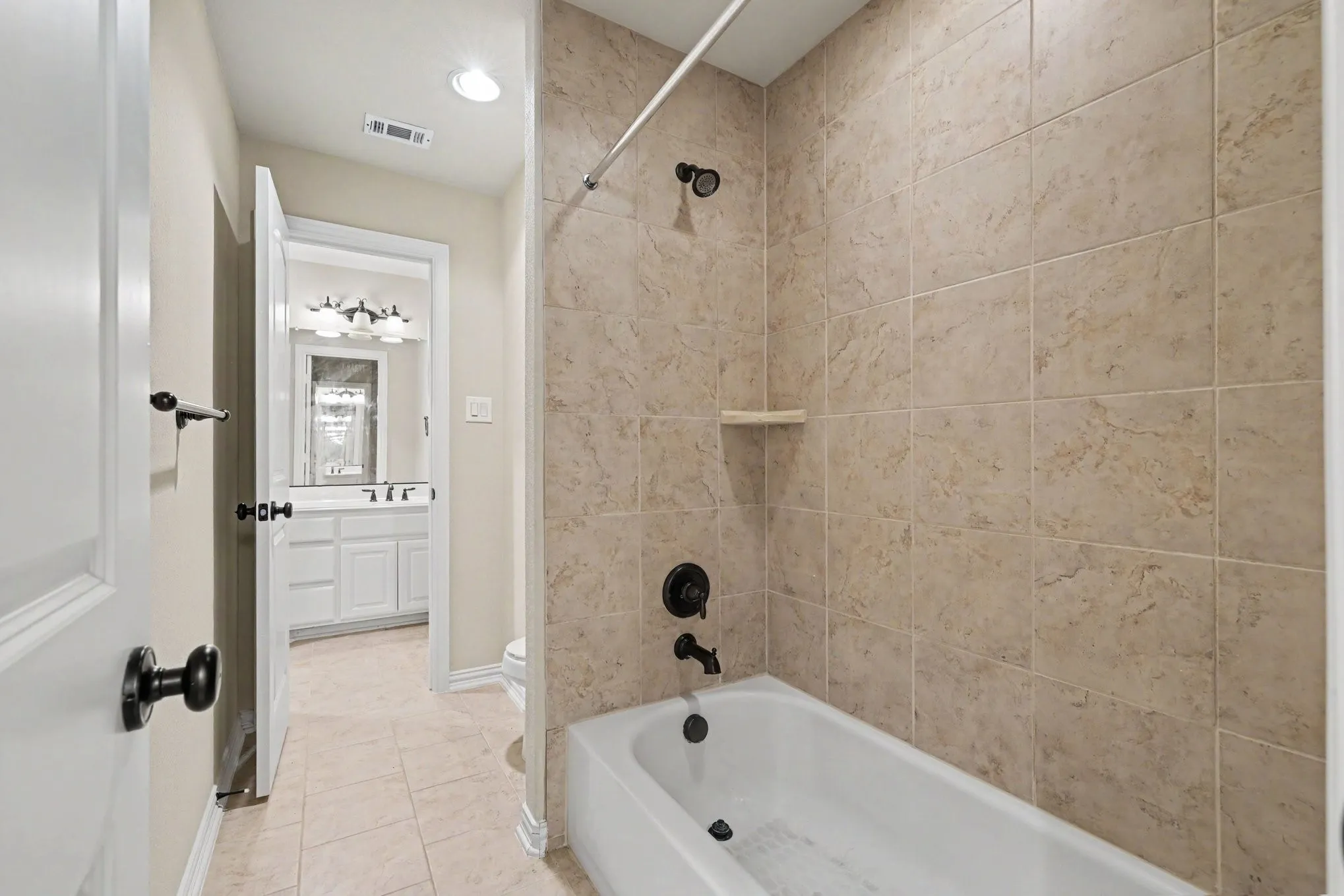 Bathtub with matte black fixtures, full-height wall tiling, and a built-in shelf- jack and jill bathroom