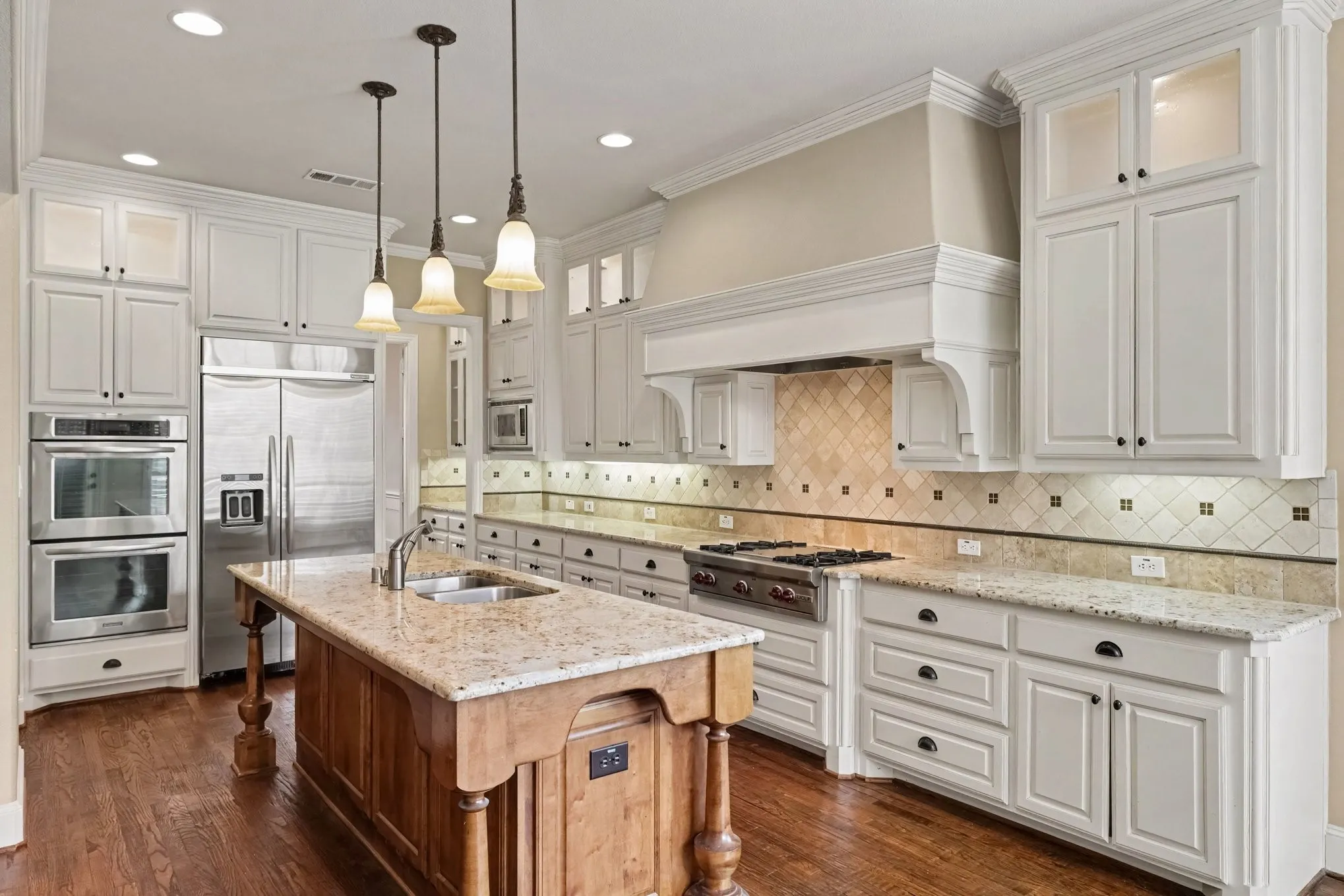 White cabinetry with dark hardware, recessed lighting, wood-finish flooring, and custom refrigerator