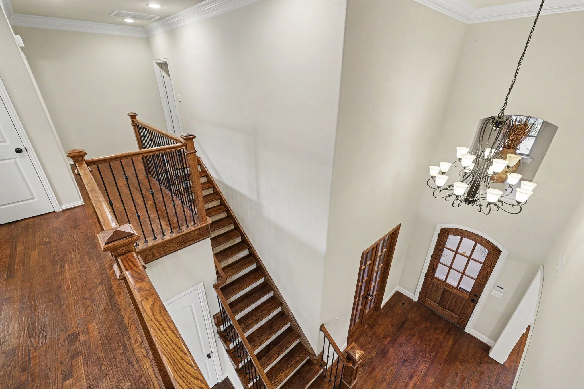 Two-story entryway with a wood-finish staircase featuring wrought iron balusters, a wood-finish front door with glass panels, and a multi-arm chandelier