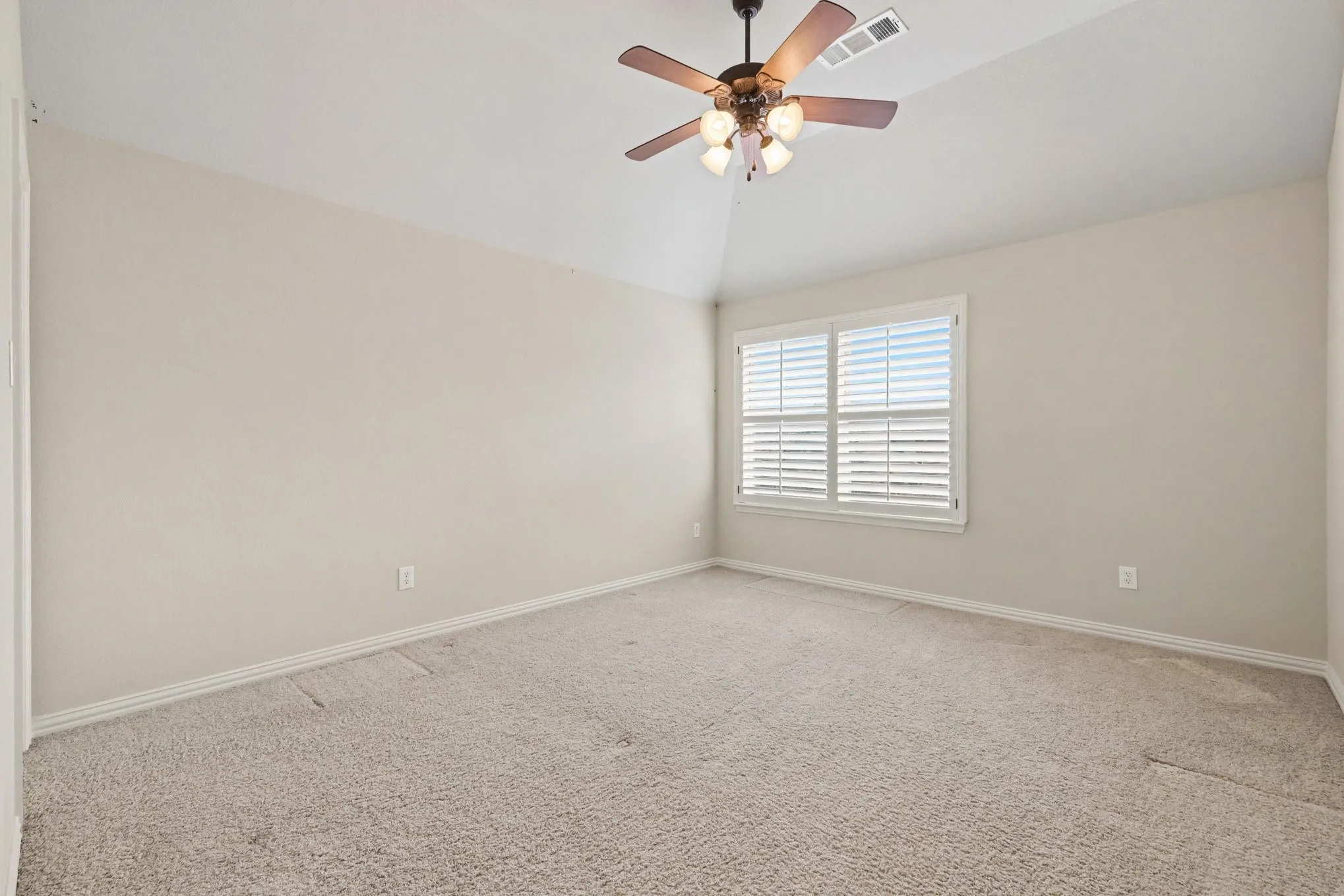 Vaulted ceiling with a ceiling fan light fixture, window with plantation shutters, and light-toned carpet flooring