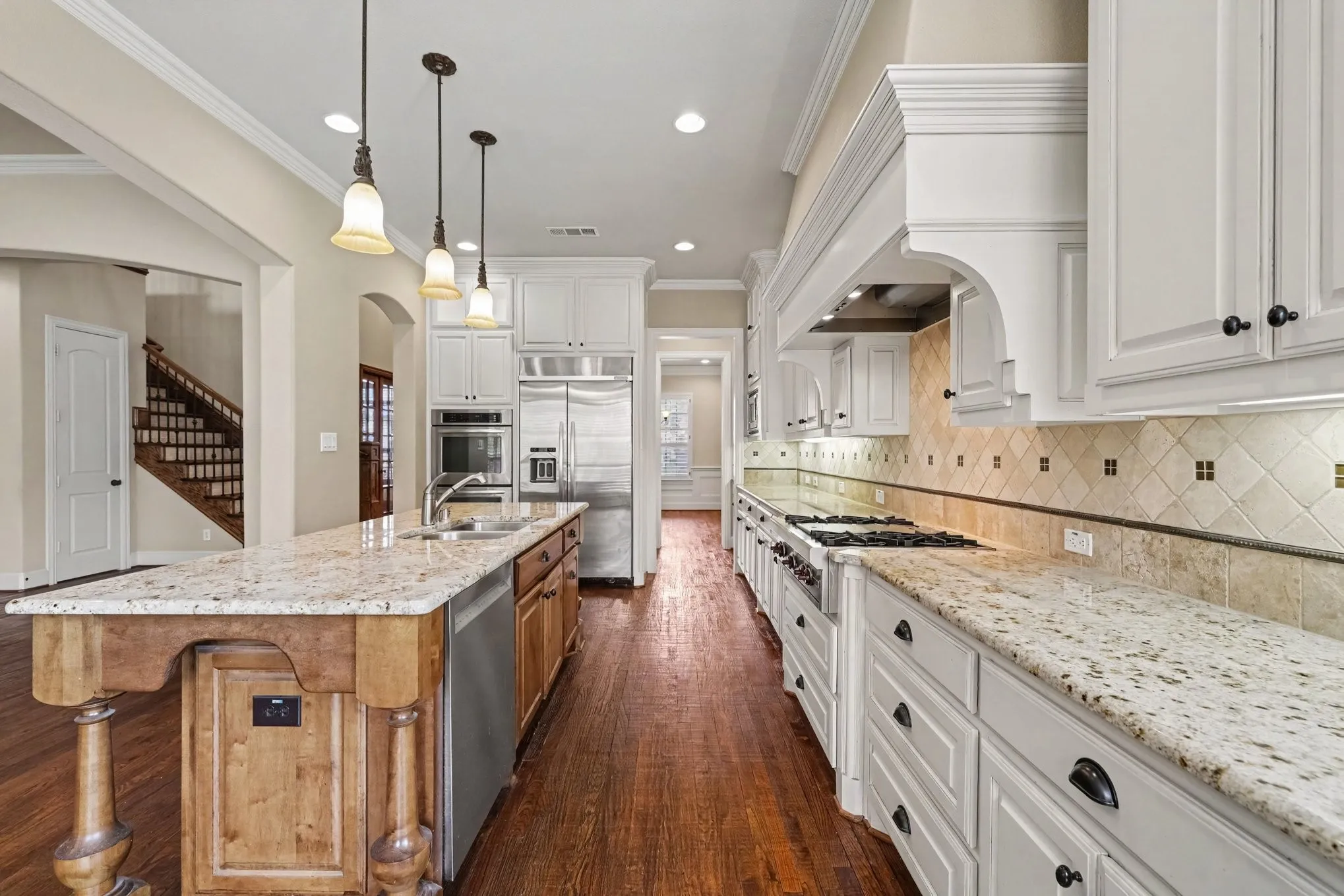 Hardwood flooring, light-toned countertops, white cabinetry, stainless steel appliances, and a tiled backsplash
