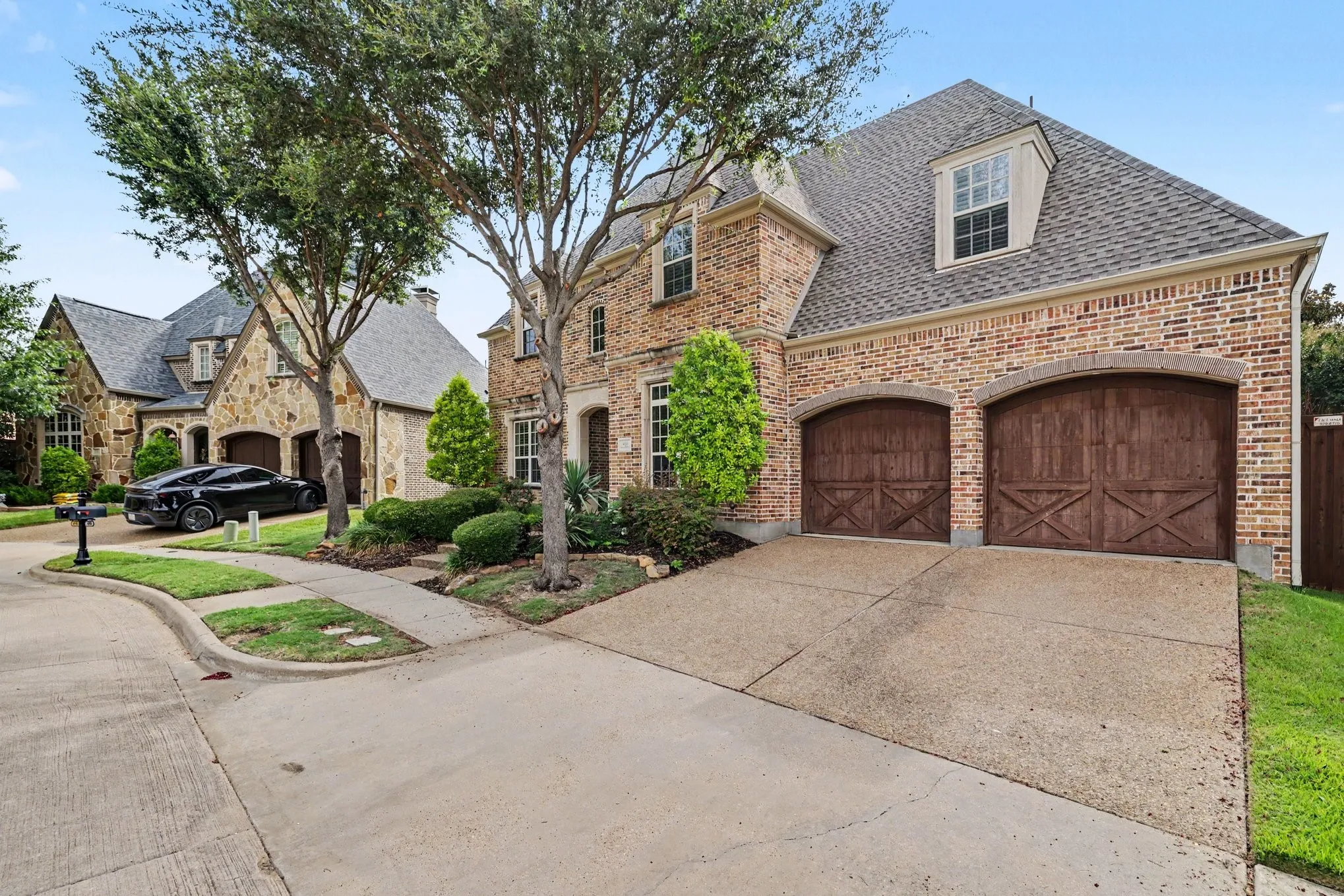 Brick exterior with stone accents, two arched wood-finish garage doors, concrete driveway, and dormer windows