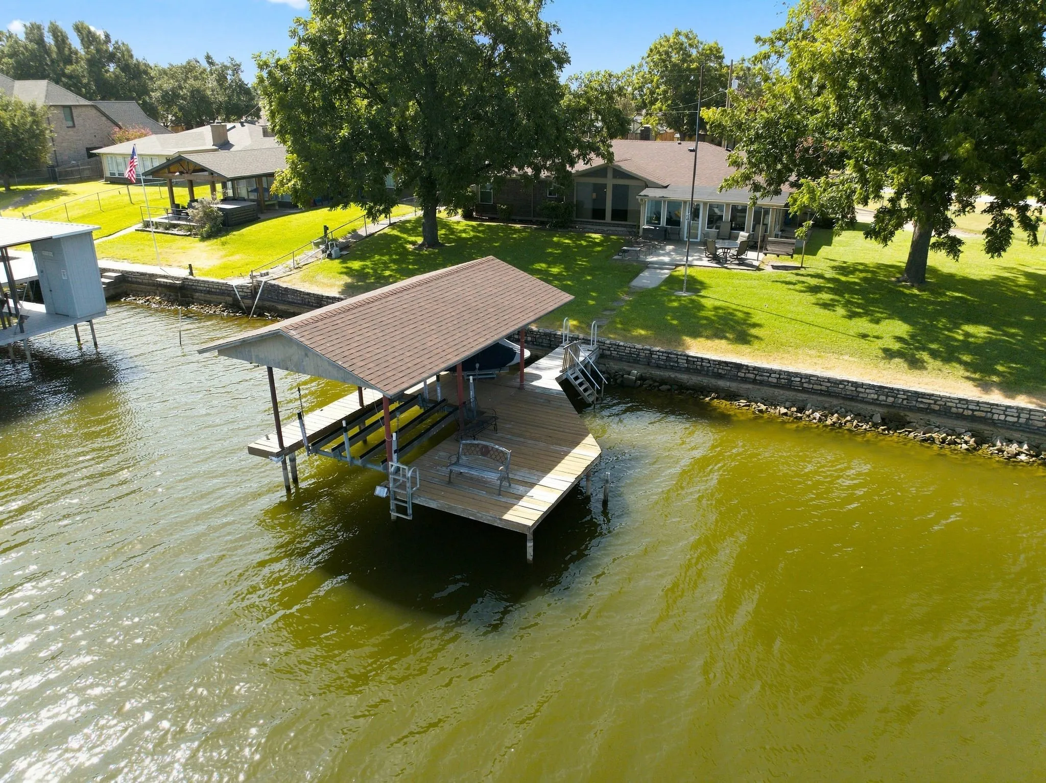 Waterfront property featuring a covered boat dock, direct water access with ladders, a stone retaining wall, and a sloped grass lawn