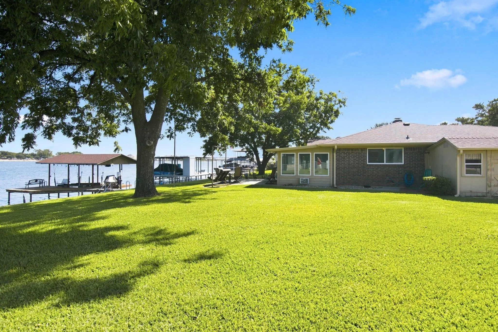 Expansive lawn area, mature shade trees, direct water access, covered dock structure, and additional boat slips