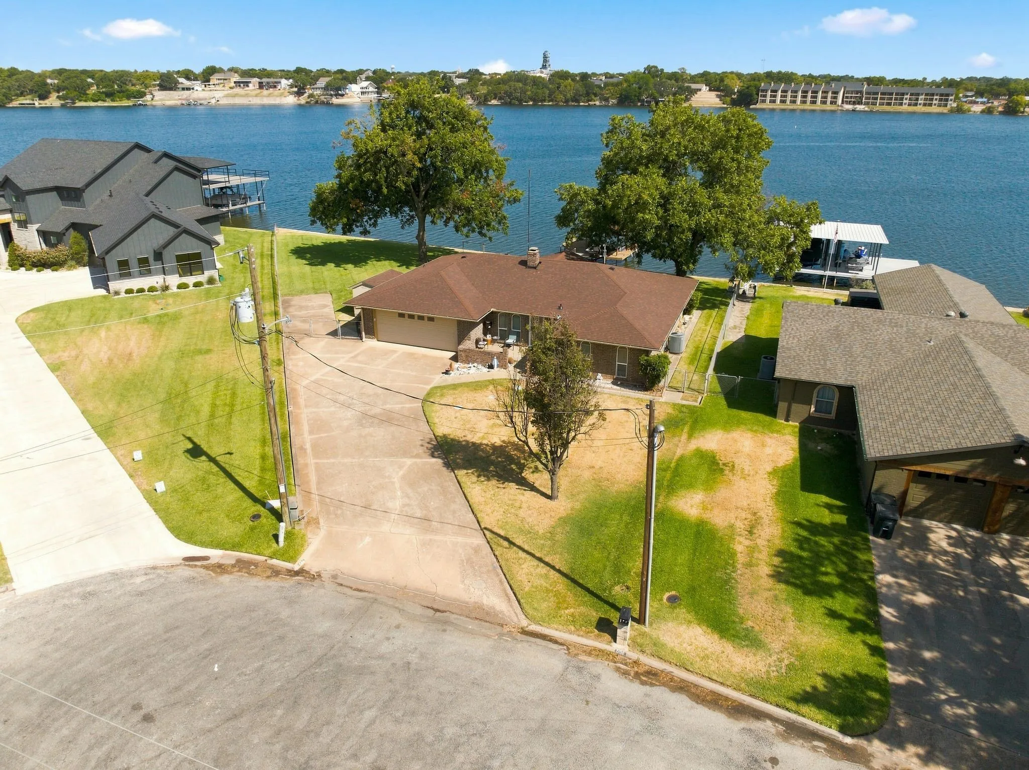 Waterfront property featuring a private boat dock, expansive driveway, attached garage, and mature trees
