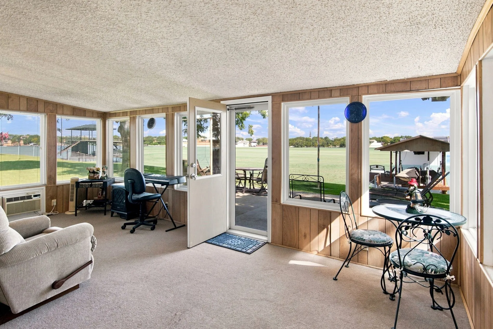 Carpeted sunroom with extensive window placement, wood paneling, and an exterior door
