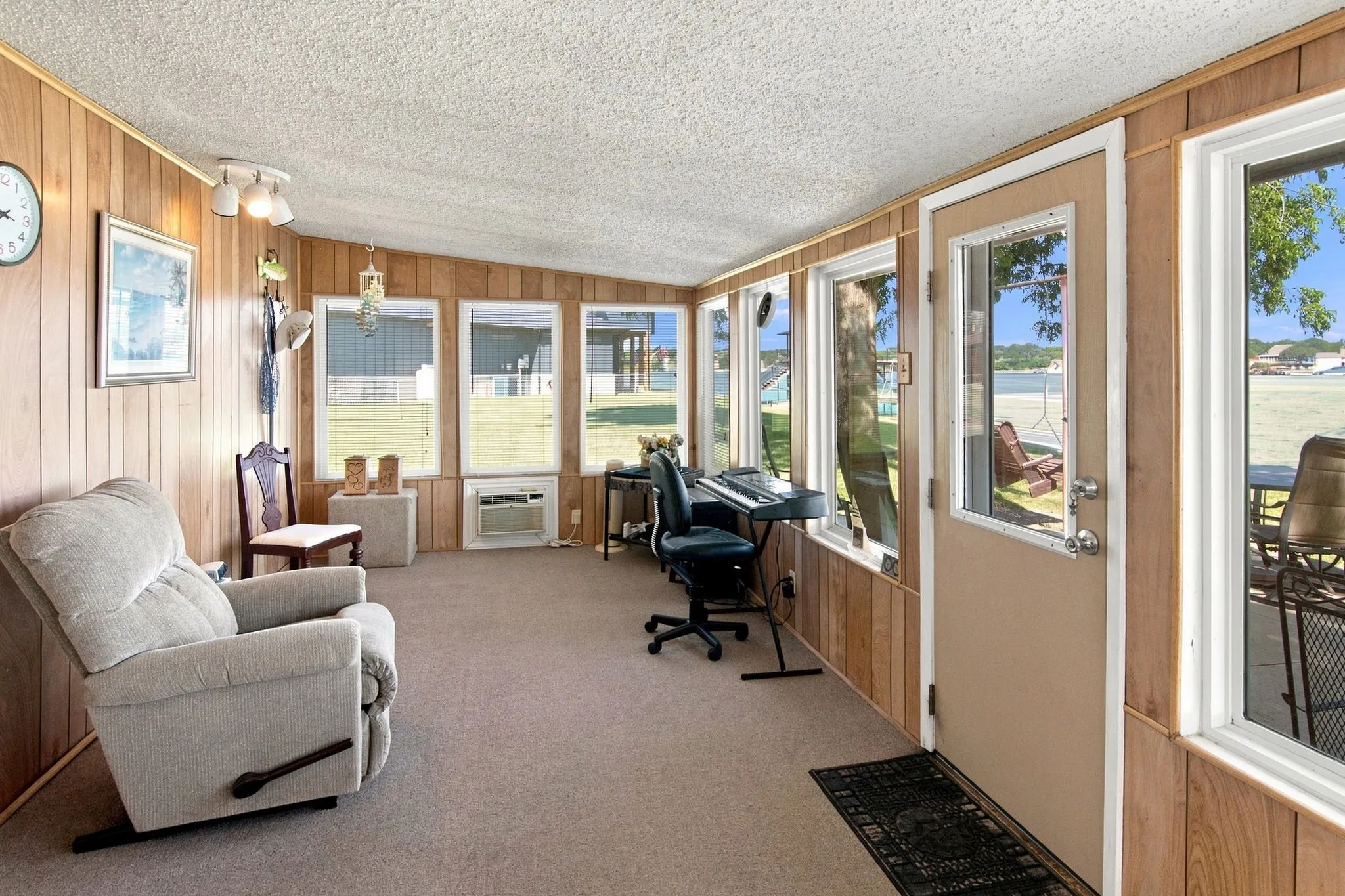 Sunroom featuring wood-paneled walls, multiple windows, a ceiling fan with light, an air conditioning unit, and carpeting