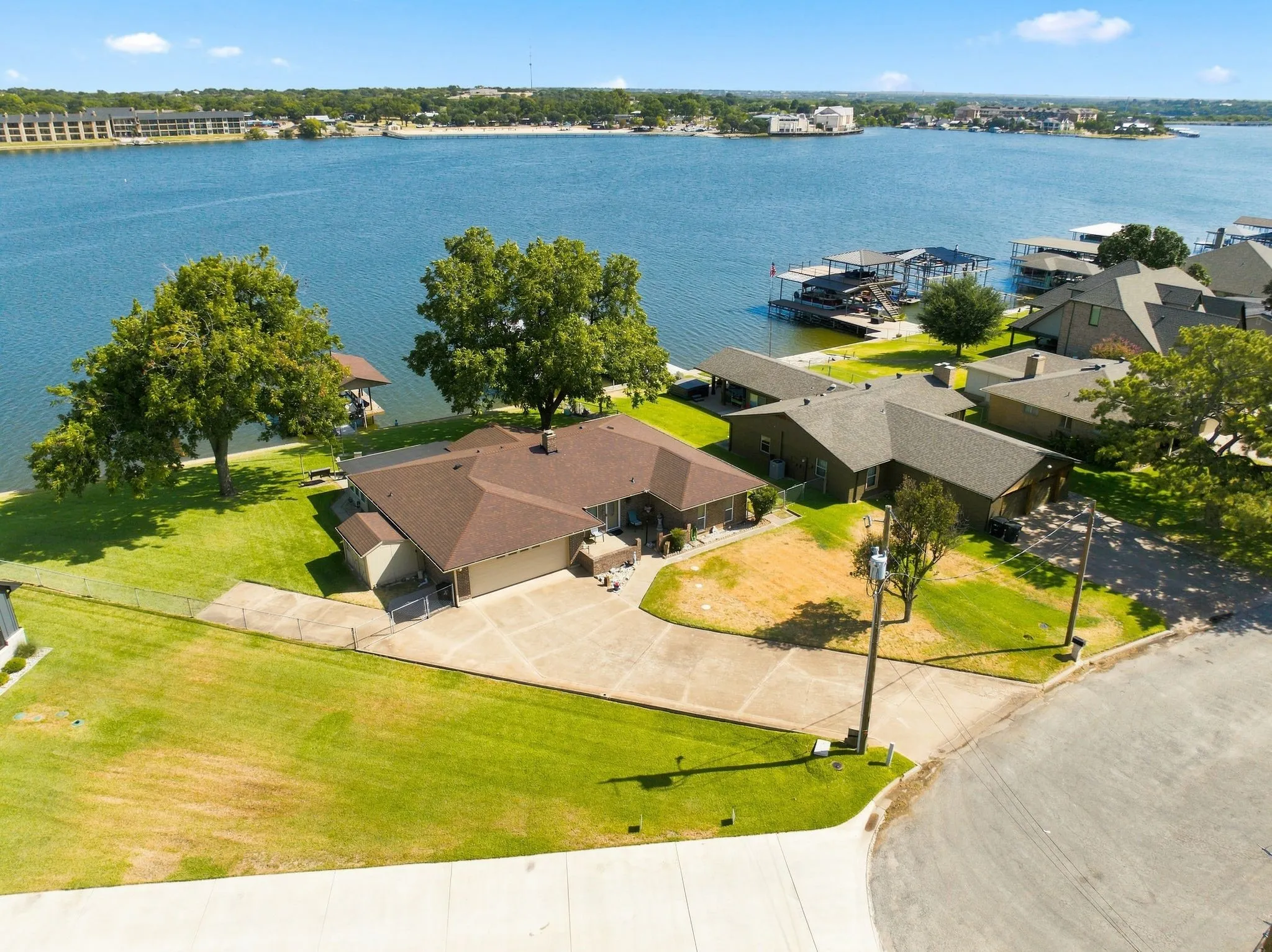 Waterfront property featuring a private boat dock, mature trees, and an expansive paved driveway
