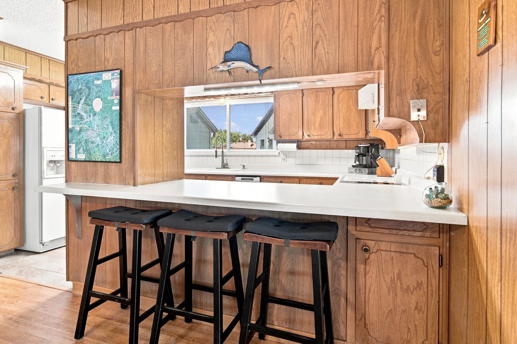 Pass-through window, built-in cabinetry, white countertop, white tile backsplash, and light wood-paneled walls