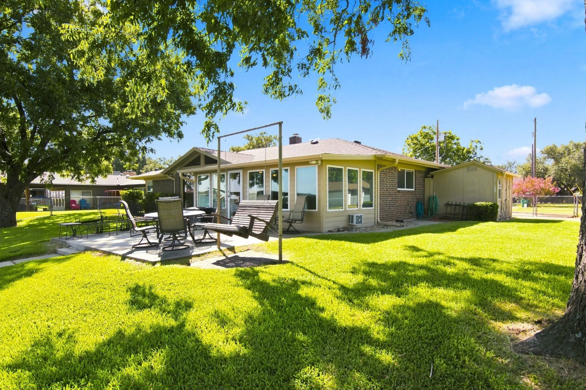 Expansive backyard featuring a manicured lawn, established shade trees, and a paved patio area