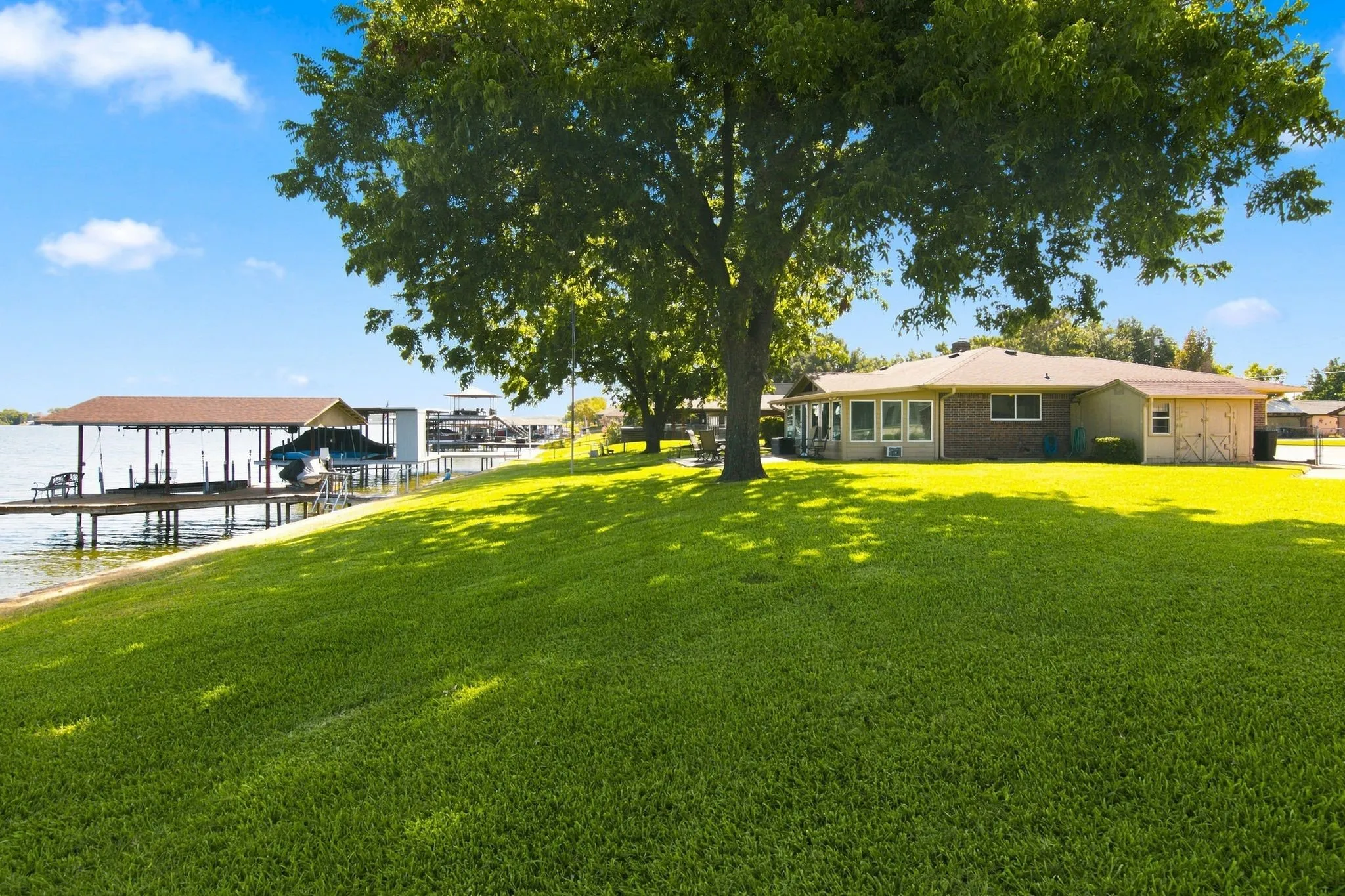Expansive green lawn with mature shade trees, waterfront access, private covered boat dock, and multi-pane windows