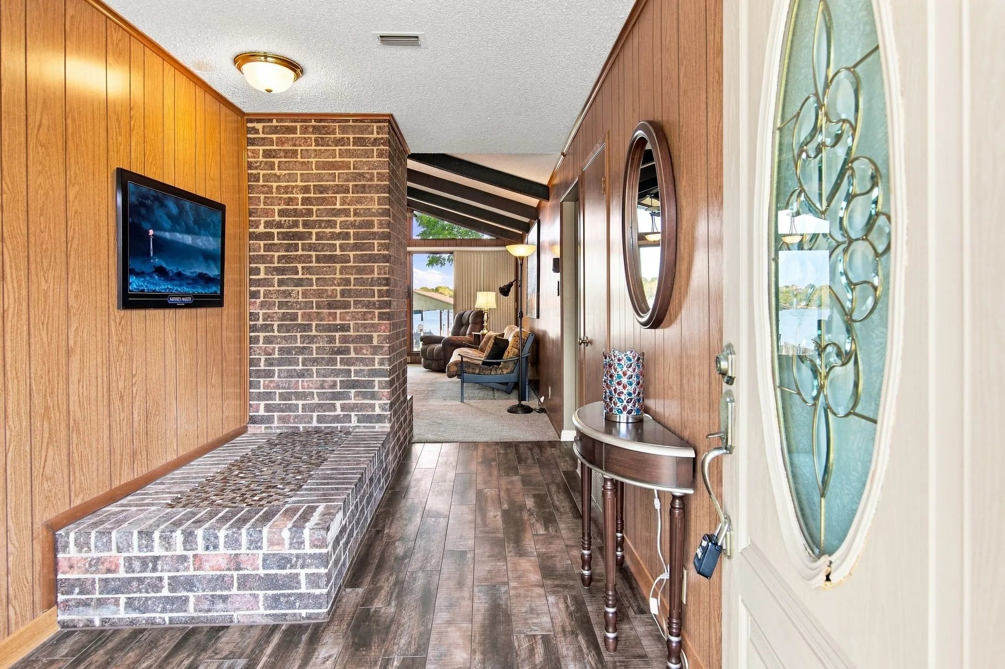 Wood-finish flooring throughout the entry, brick-clad architectural feature, and a door with decorative glass inlay