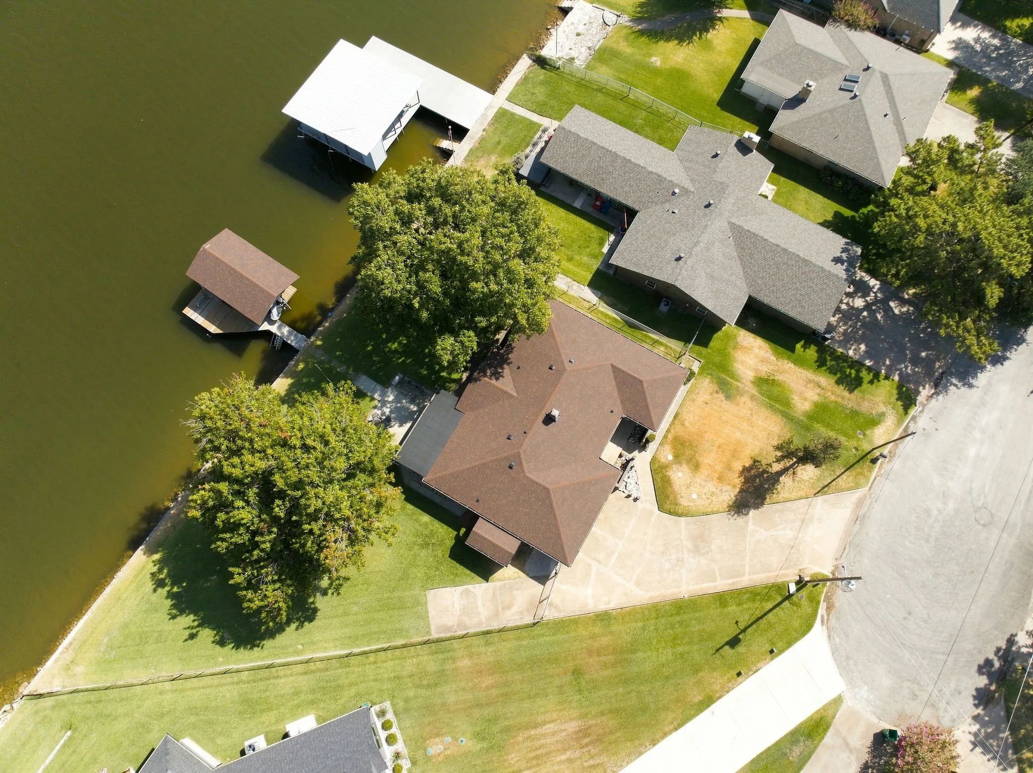 Waterfront property featuring a private boat dock, mature trees, and a spacious green lawn