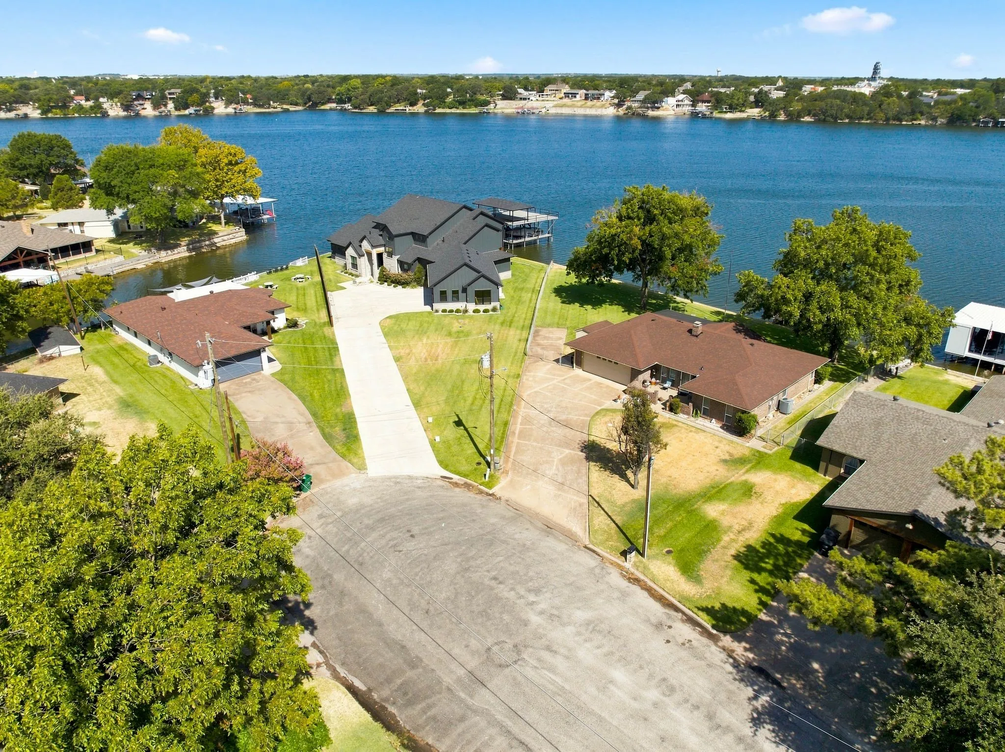 Waterfront property featuring a contemporary residence with multiple balconies, a long paved driveway, and manicured green spaces