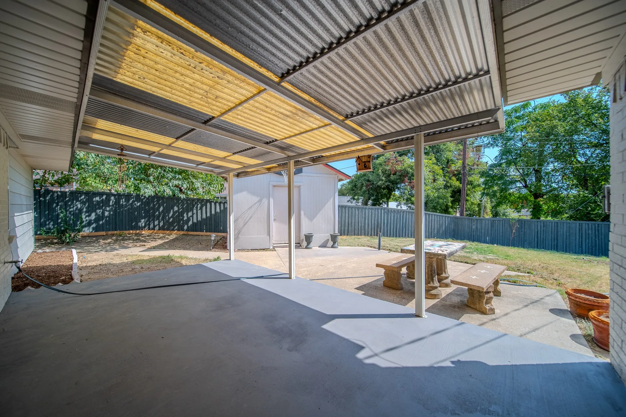 Expansive covered patio with corrugated metal roofing, concrete slab, and structural support pillars