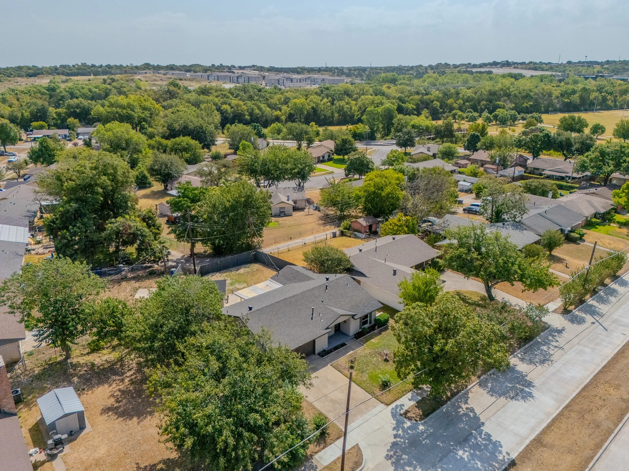 Aerial perspective featuring a residential street with concrete sidewalks, mature trees, and single-story properties