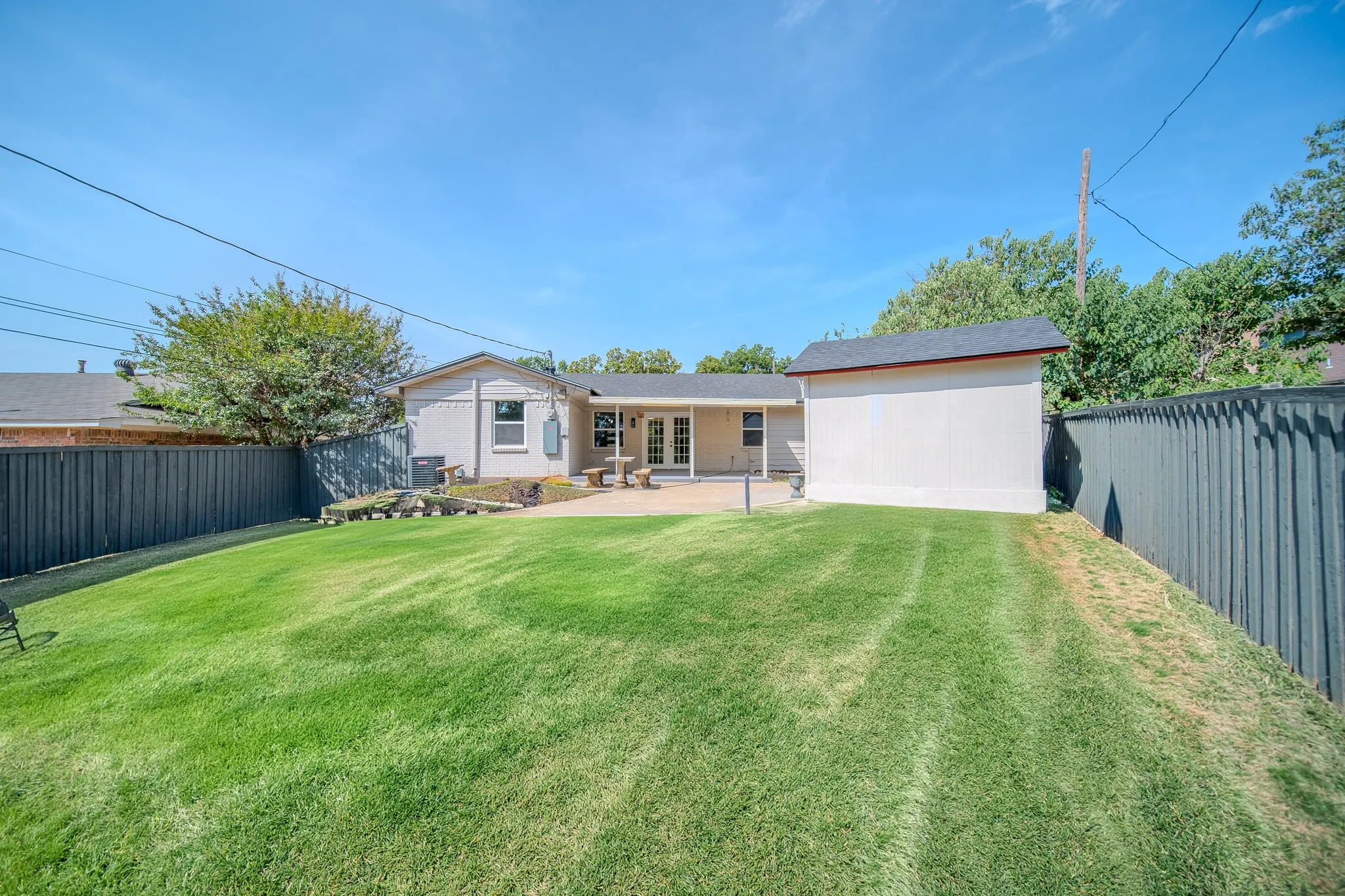 Expansive backyard featuring a manicured lawn, a paved patio, and a detached storage shed