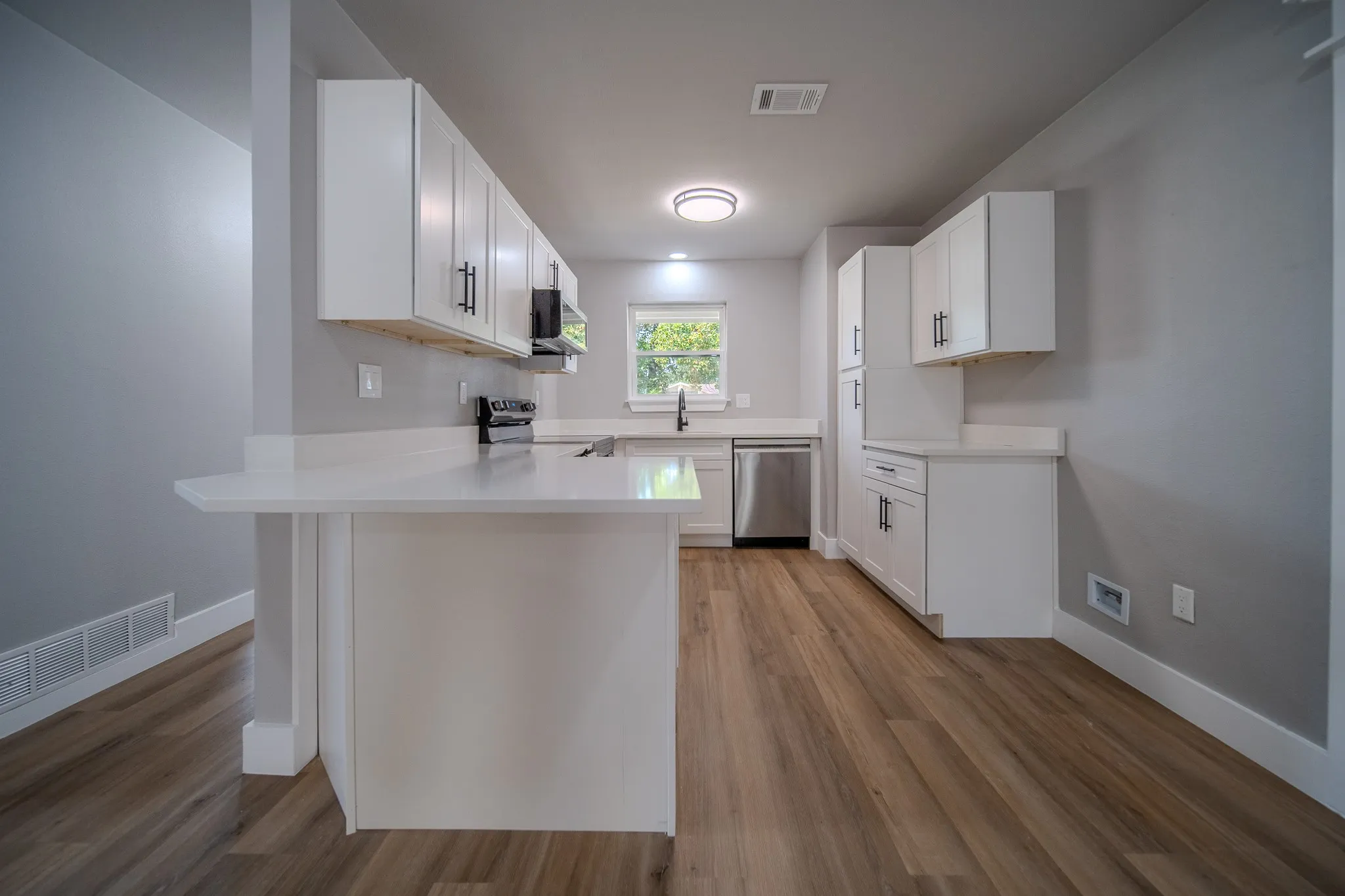 Kitchen featuring white cabinetry, light-colored countertops, stainless steel appliances, and wood-finish flooring