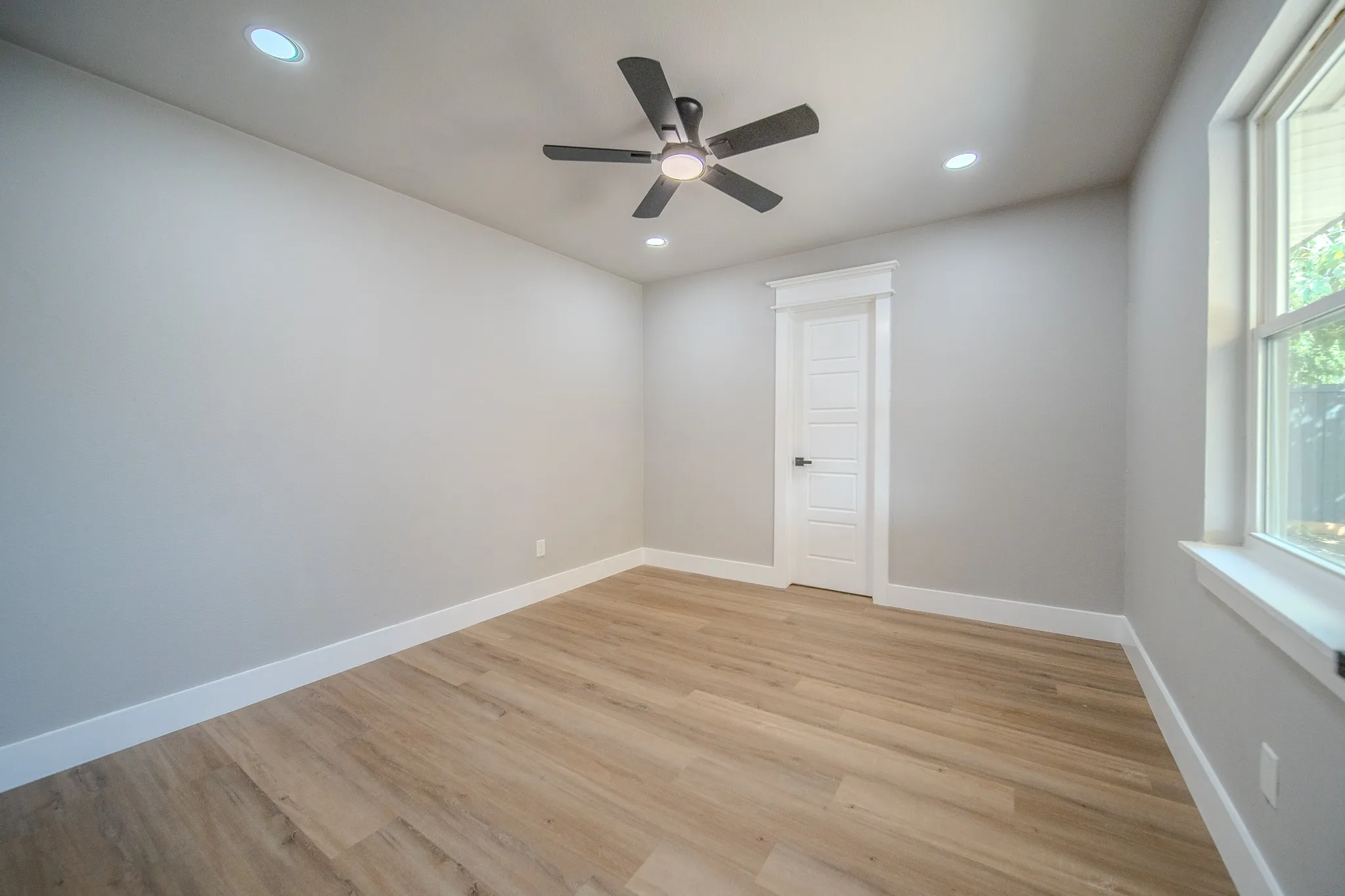 Recessed lighting, wood-finish flooring, ceiling fan, white trim, and a paneled door with dark hardware