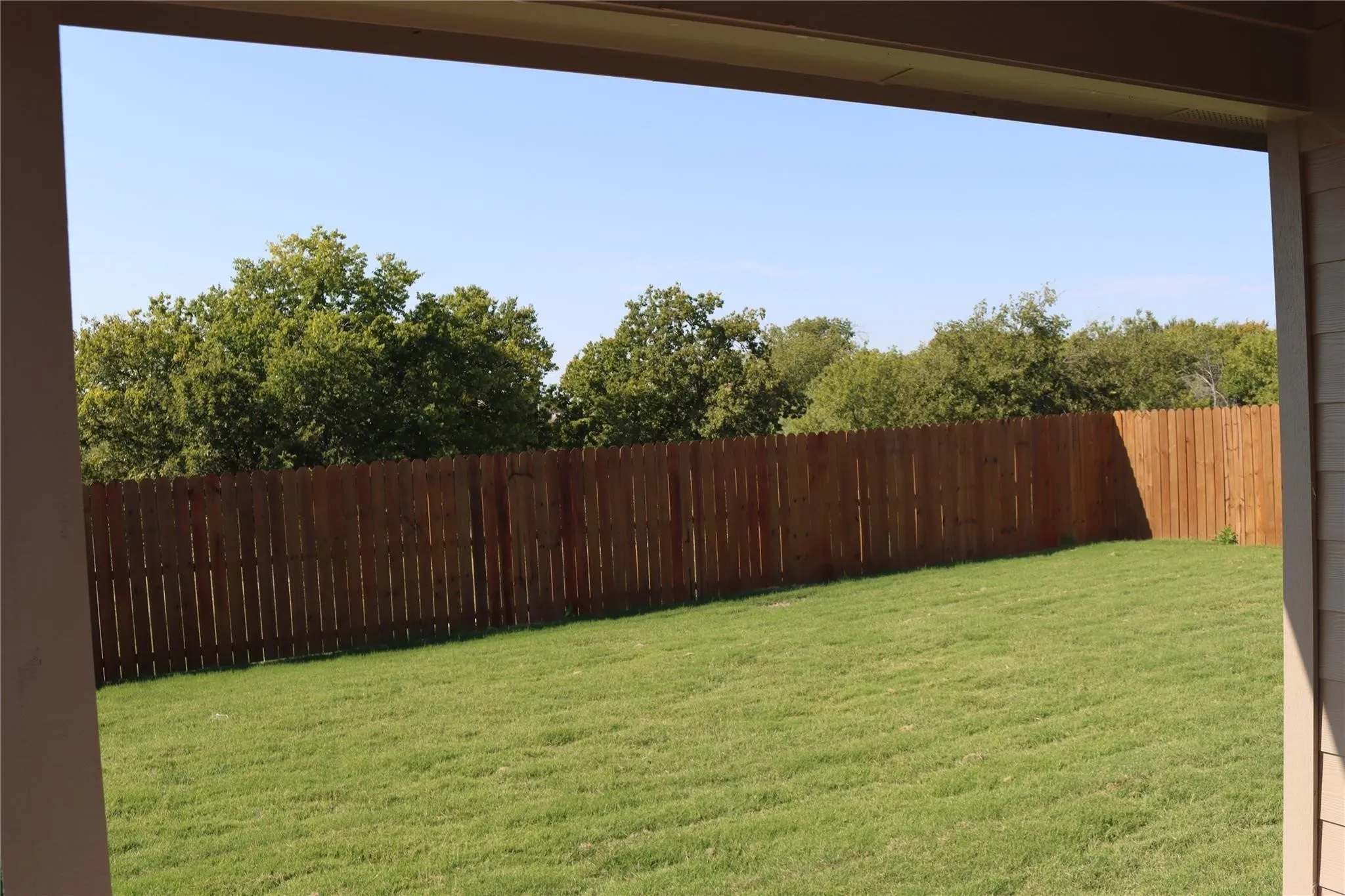 Expansive backyard featuring a manicured lawn, a full wood fence perimeter, and mature trees