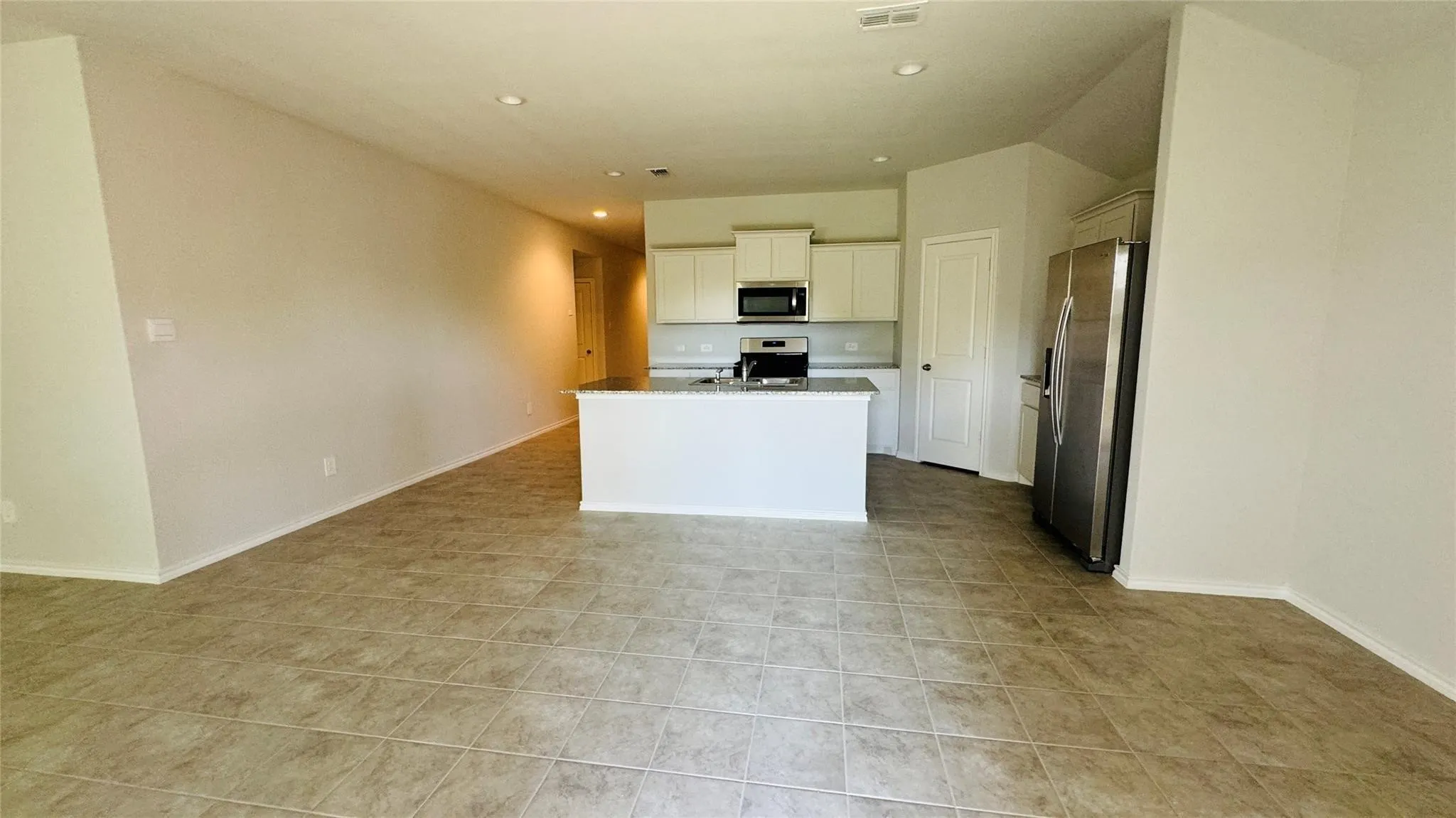 Tile flooring throughout, recessed lighting, kitchen island with built-in sink, stainless steel appliances, and upper cabinetry