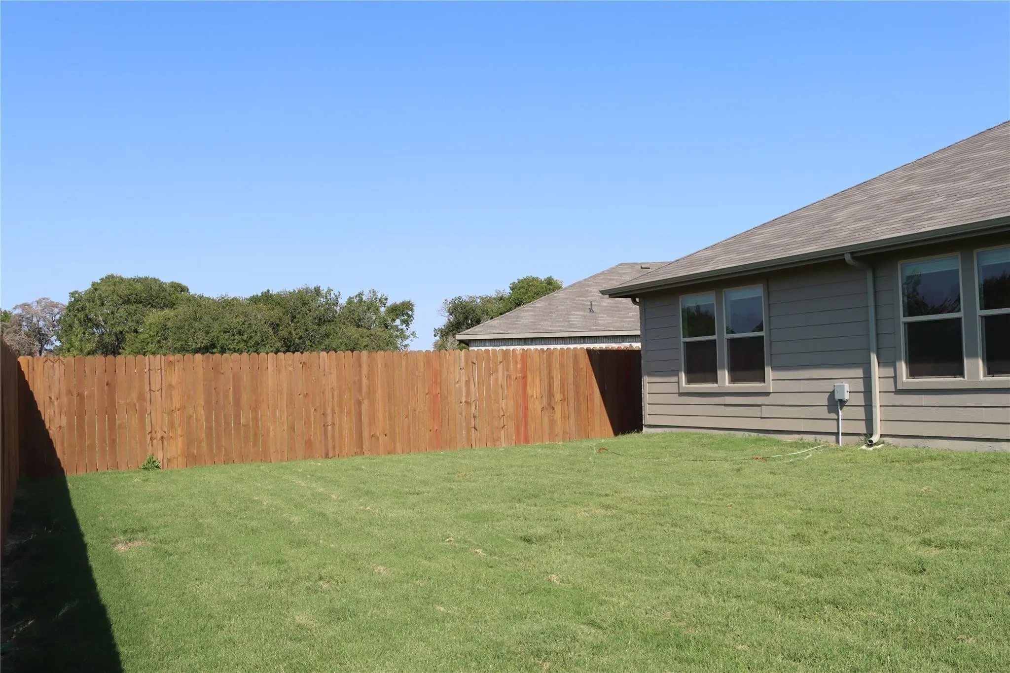 Expansive fenced backyard with a manicured lawn, wood privacy fence, and multi-paned windows on the home's exterior