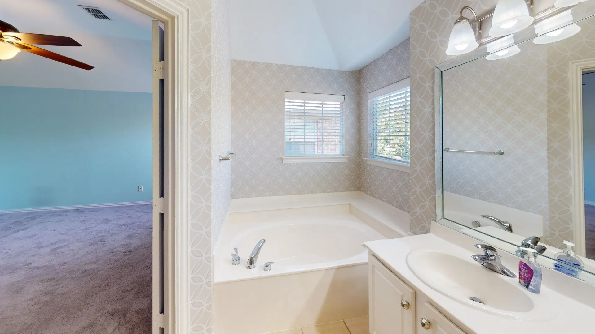 Built-in bathtub with chrome fixtures, dual windows with blinds, a vanity with an integrated sink, and an overhead lighting fixture