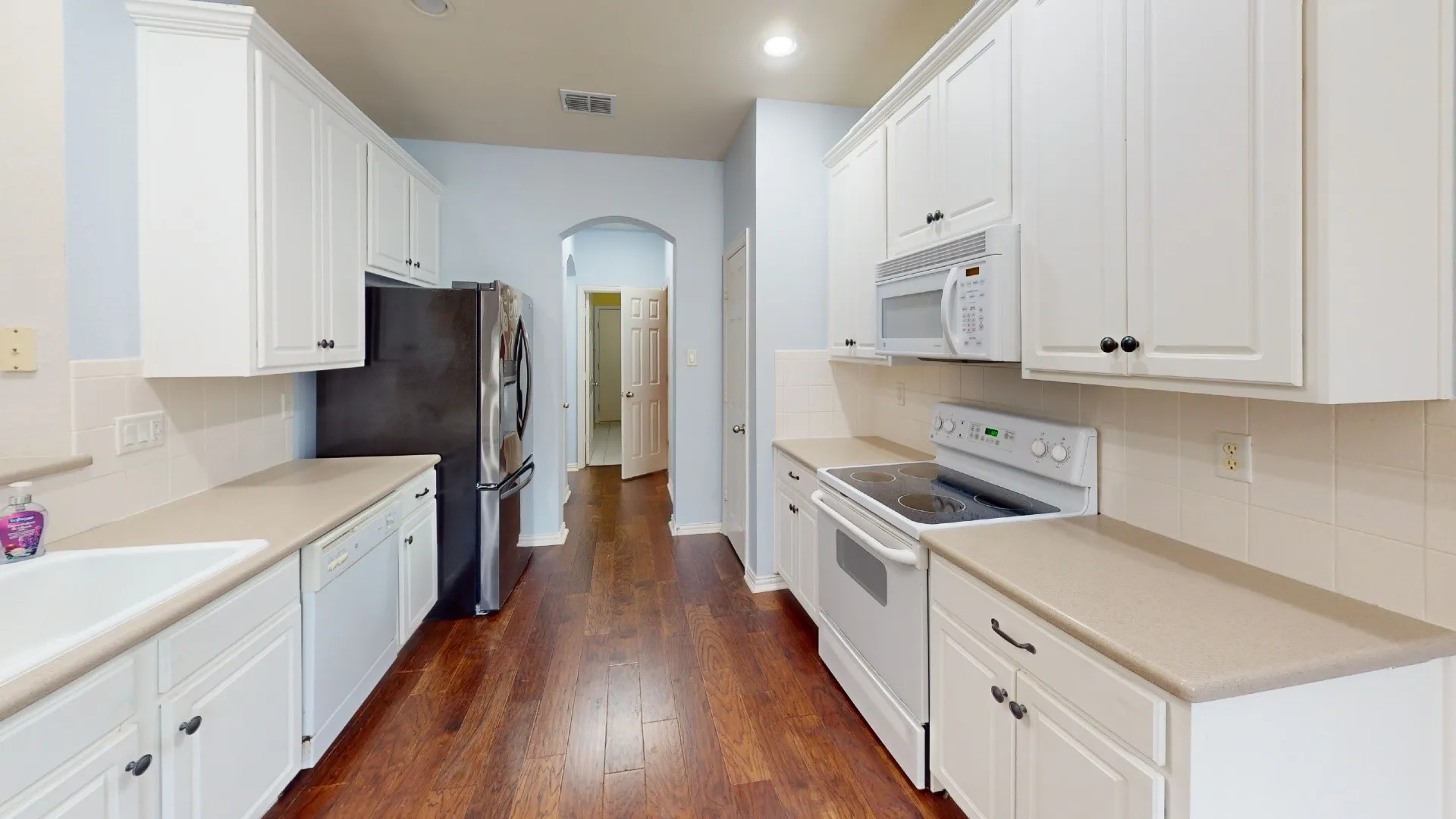 Kitchen featuring wood-finish flooring, white cabinetry, a stainless steel refrigerator, and an arched doorway