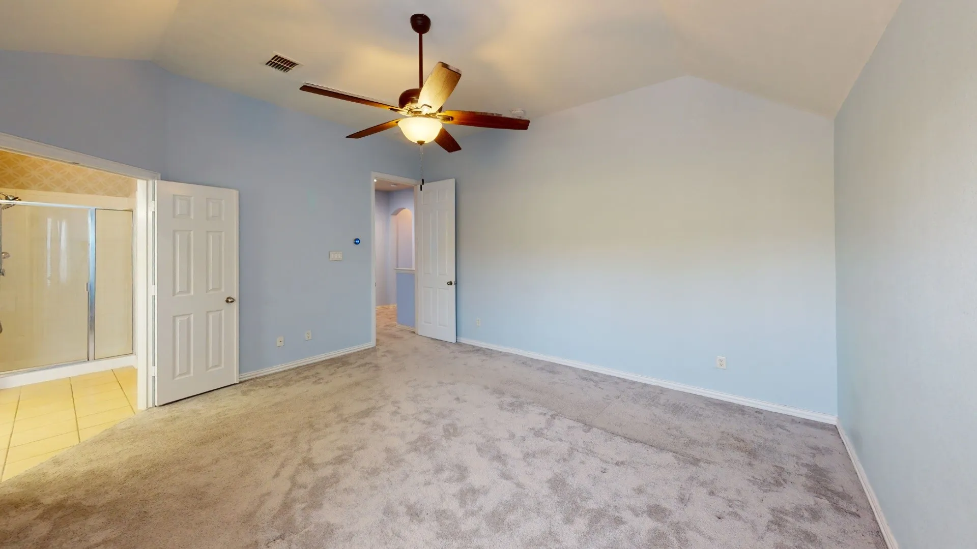 Vaulted ceiling with an attached ceiling fan, carpet flooring, and a tiled shower with a glass enclosure