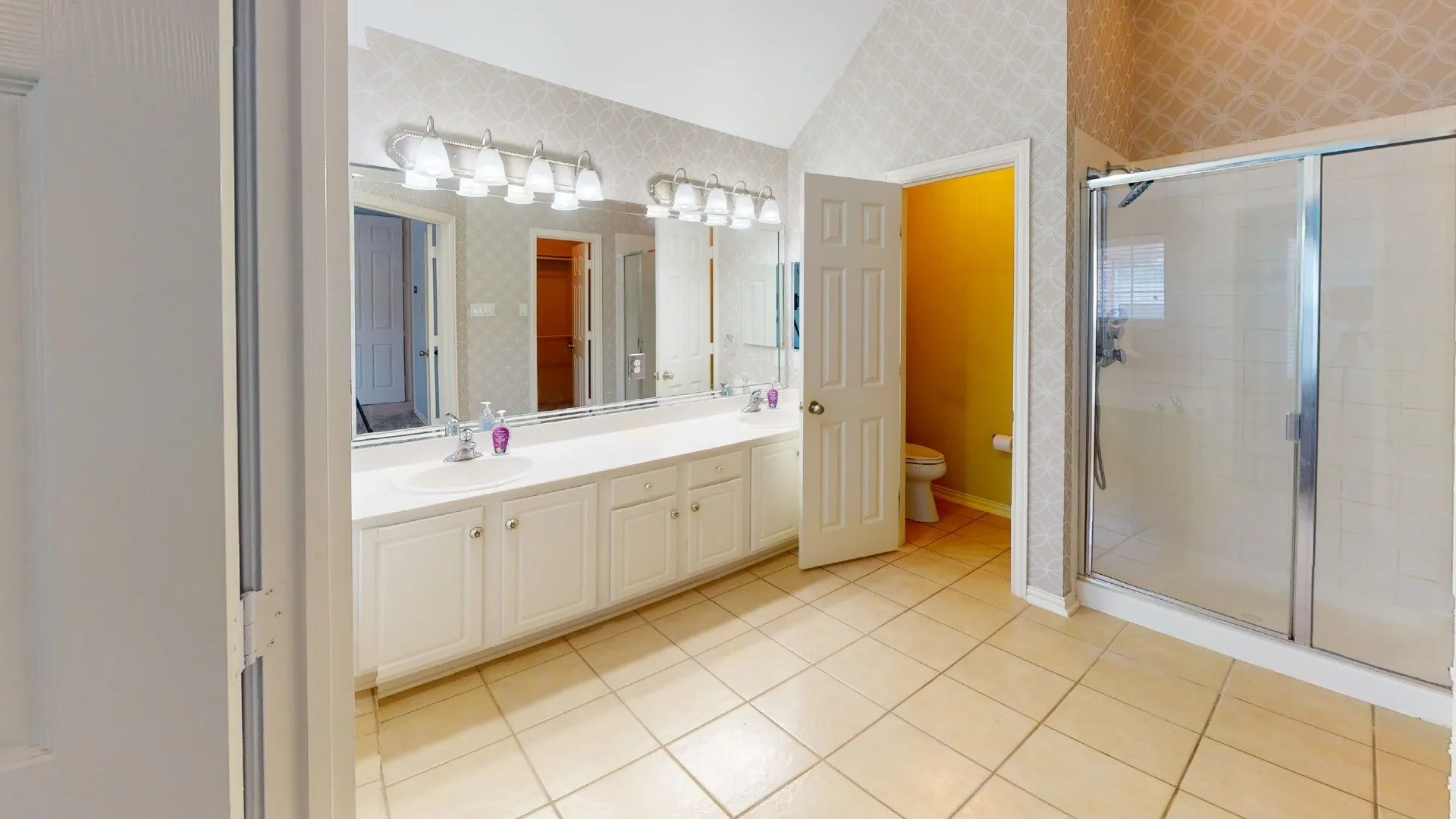 Double vanity with two sinks, tile flooring, glass-enclosed shower, and vaulted ceiling