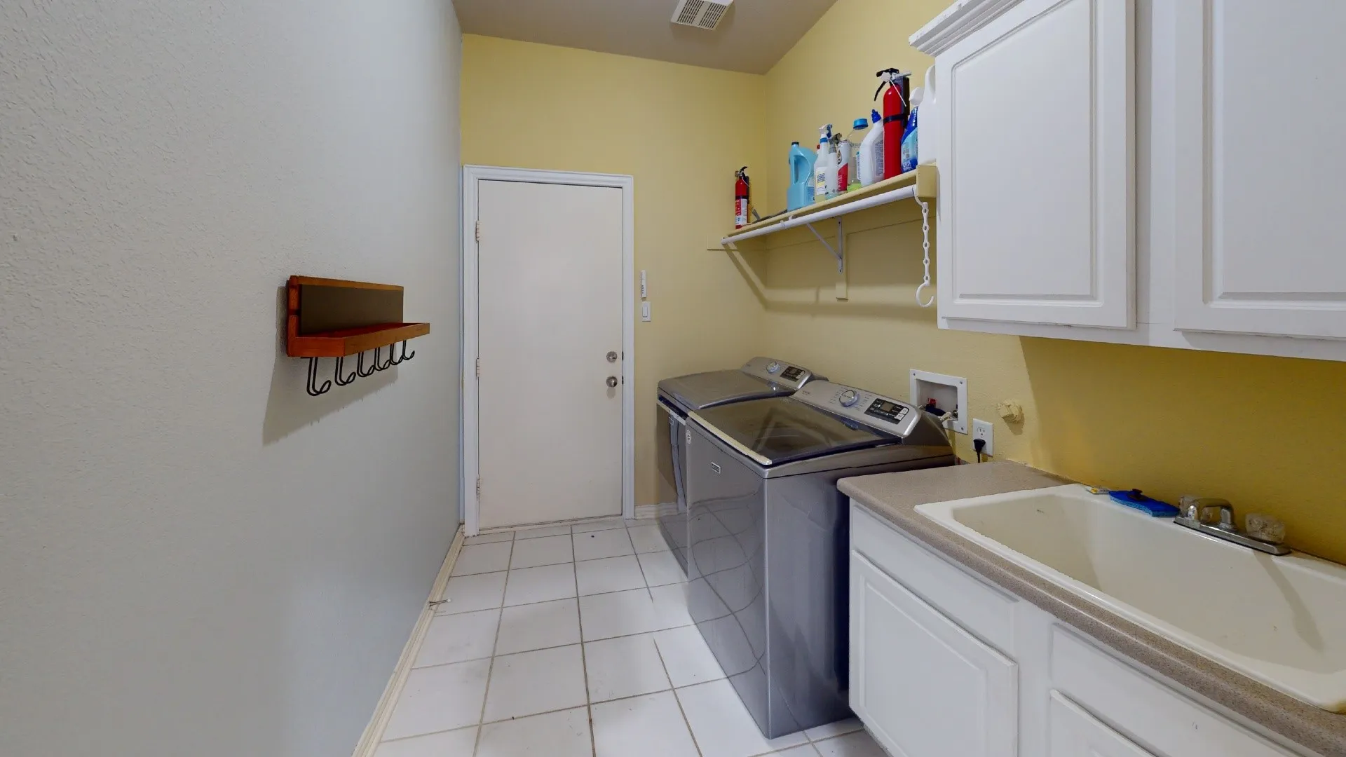 Utility space featuring tile flooring, built-in cabinetry, an integrated sink, and wall-mounted shelving