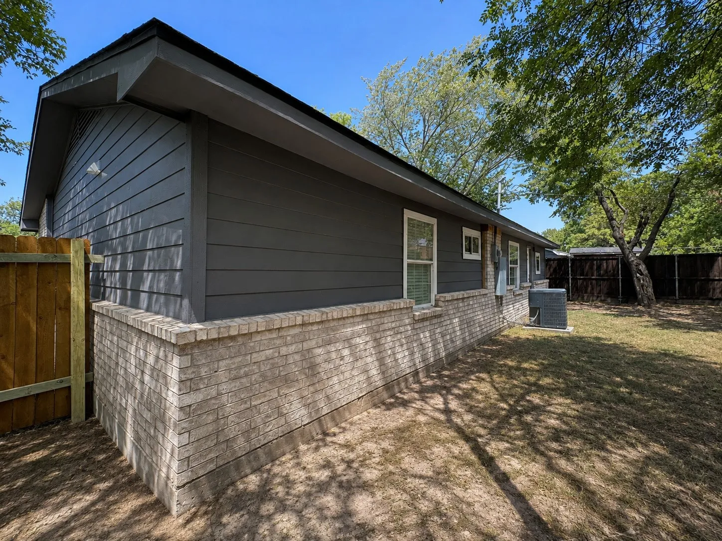 Exterior featuring horizontal siding, brick wainscoting, and a wood privacy fence