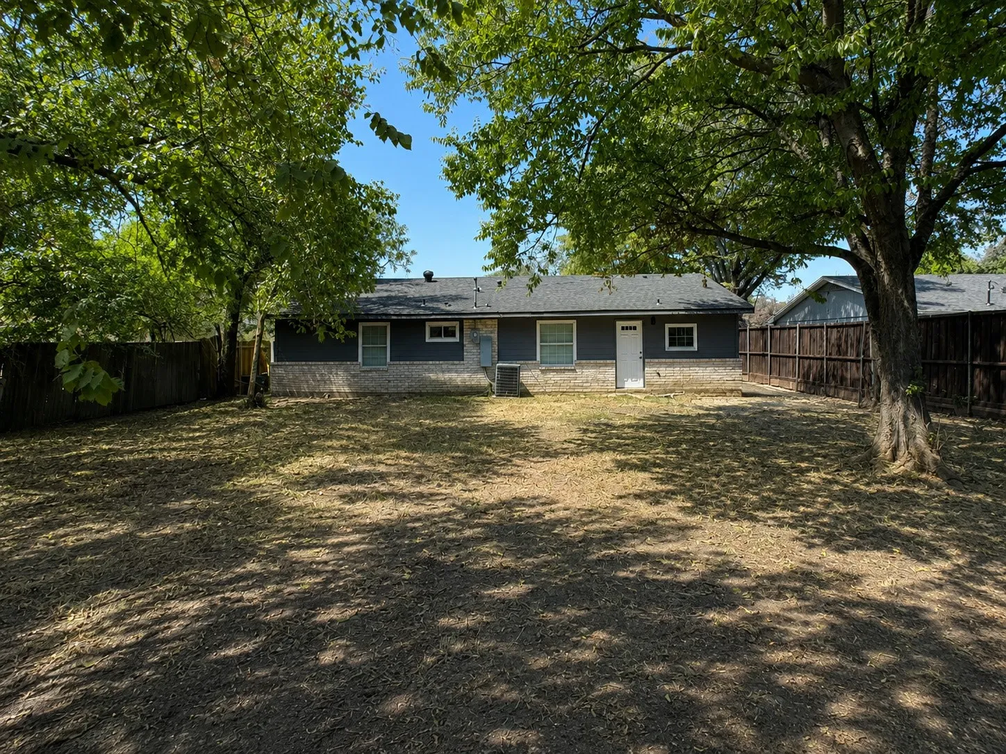 Expansive backyard featuring mature trees, dark wood fencing, and a dwelling with stone and horizontal siding