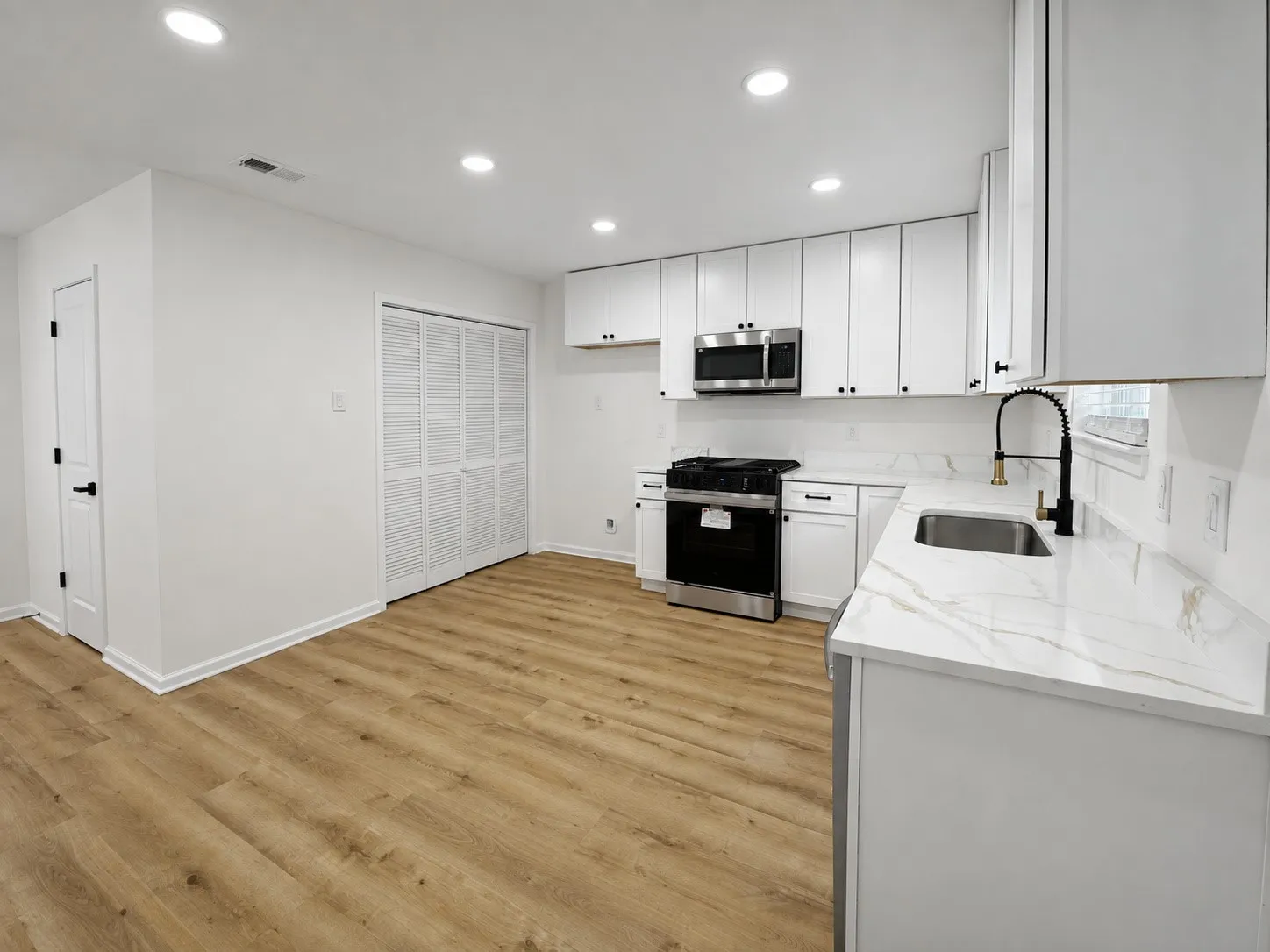 Updated kitchen featuring wood-finish flooring, white cabinetry, integrated stainless steel appliances, and a marble-look countertop with a matching backsplash