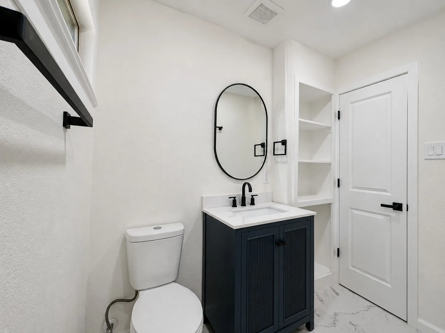Contemporary bathroom featuring a dark blue vanity with a white countertop, an oval mirror, and built-in shelving