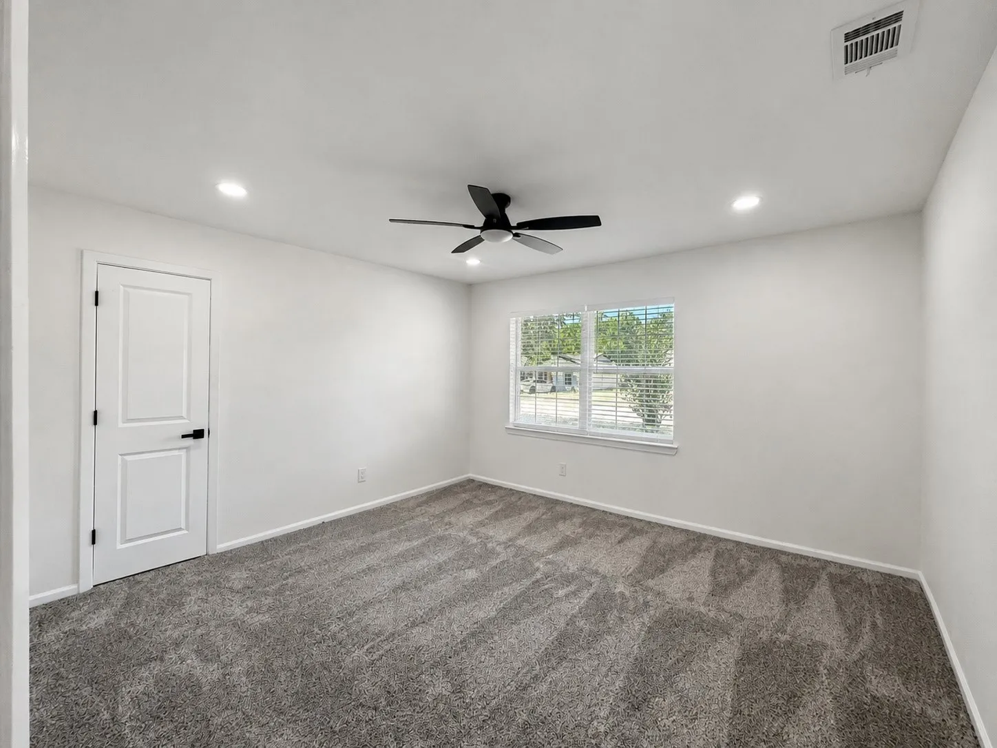 Recessed lighting, ceiling fan, white paneled door with black hardware, window with blinds, and gray carpeted flooring