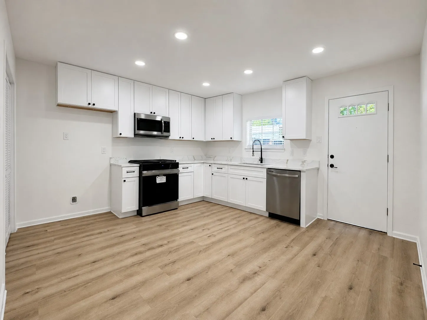 Kitchen featuring white cabinetry, stainless steel appliances, wood-finish flooring, recessed lighting, and a window above the sink