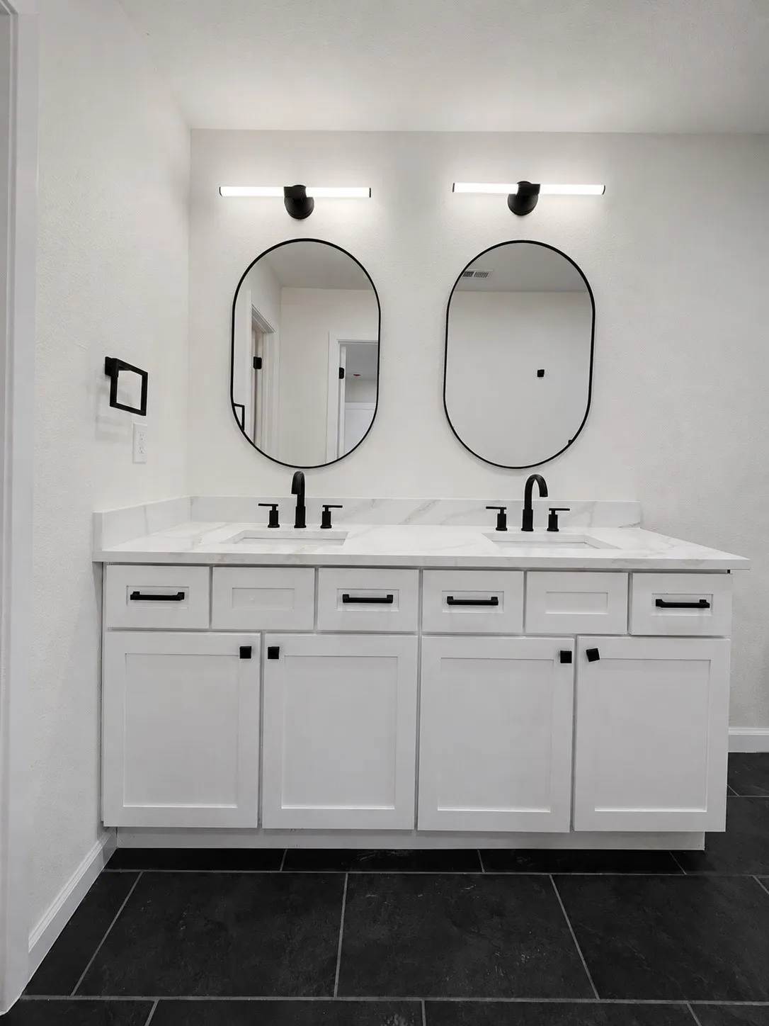 Dual vanity with white shaker-style cabinetry, matte black hardware, and a light-toned countertop